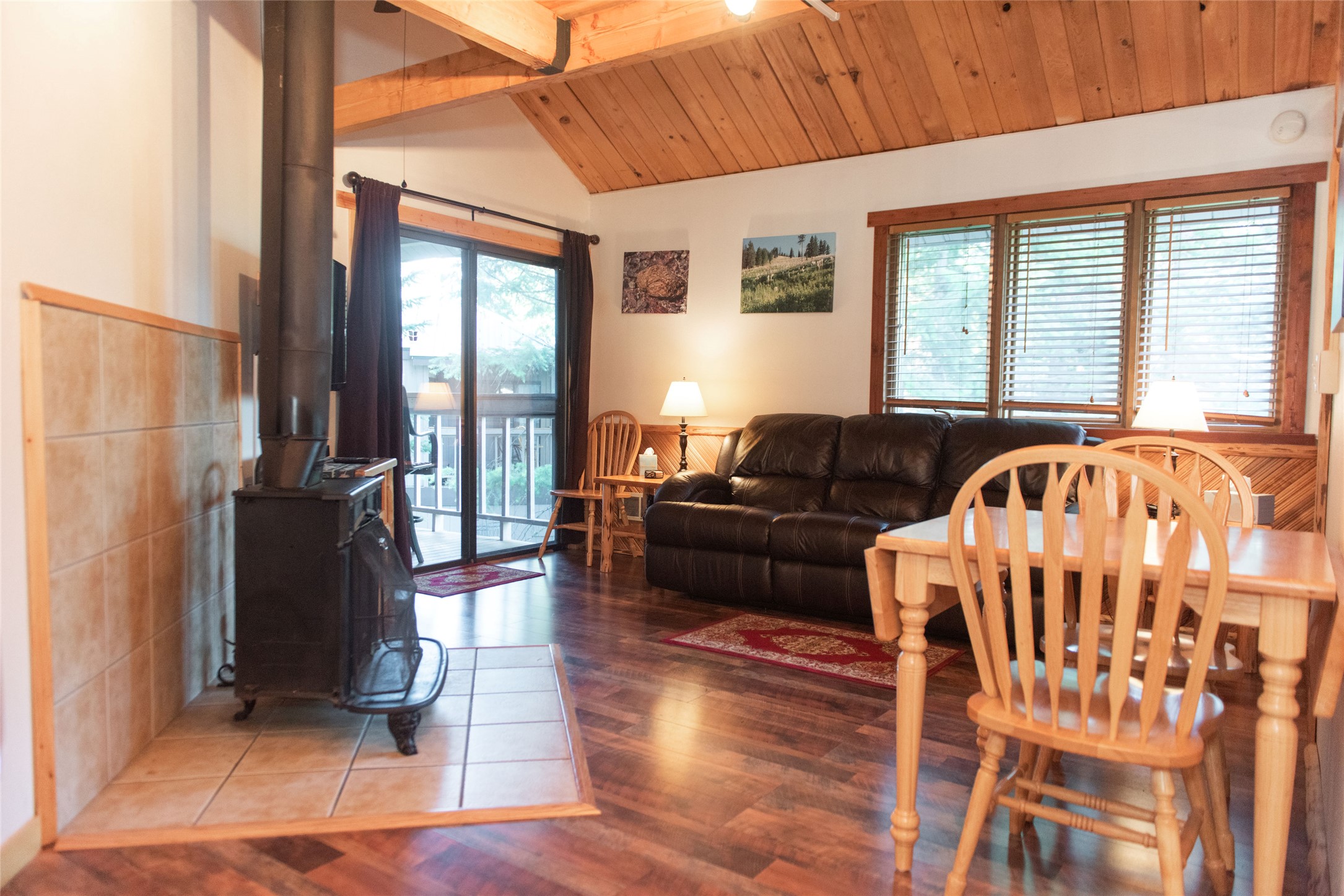 Living and dining room with a wood stove, vaulted wood ceiling, leather sofa, and balcony access.