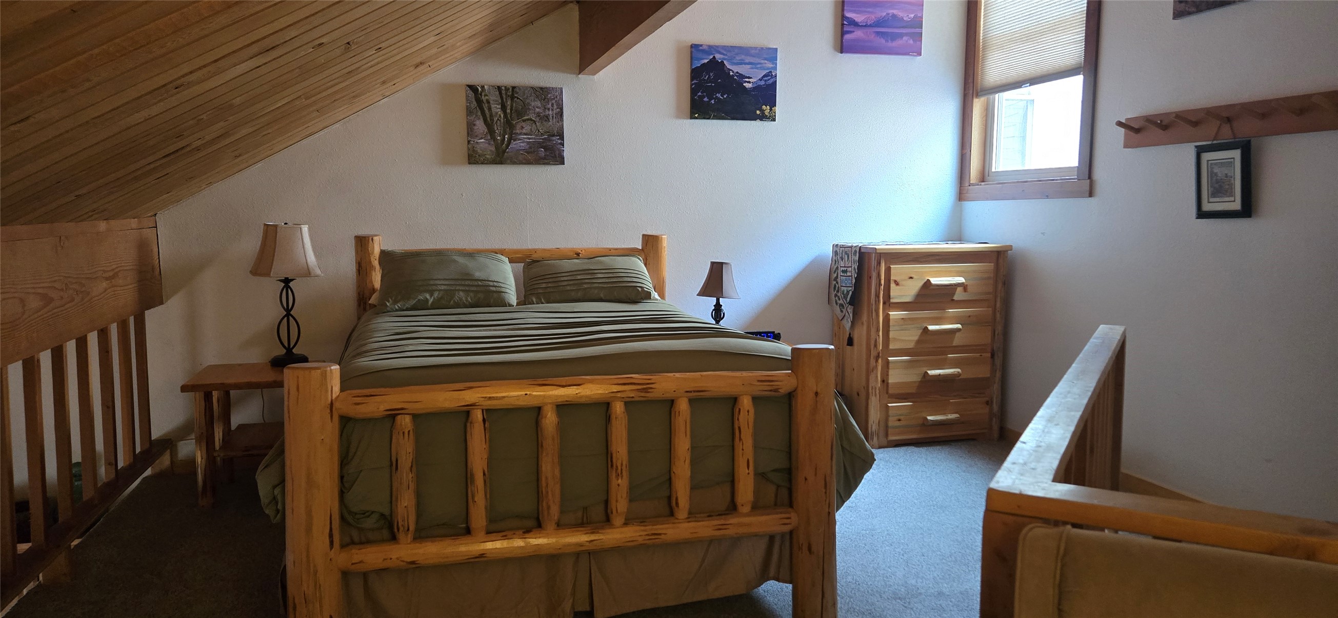 Loft bedroom with a rustic log bed beneath a sloped wood-plank ceiling.