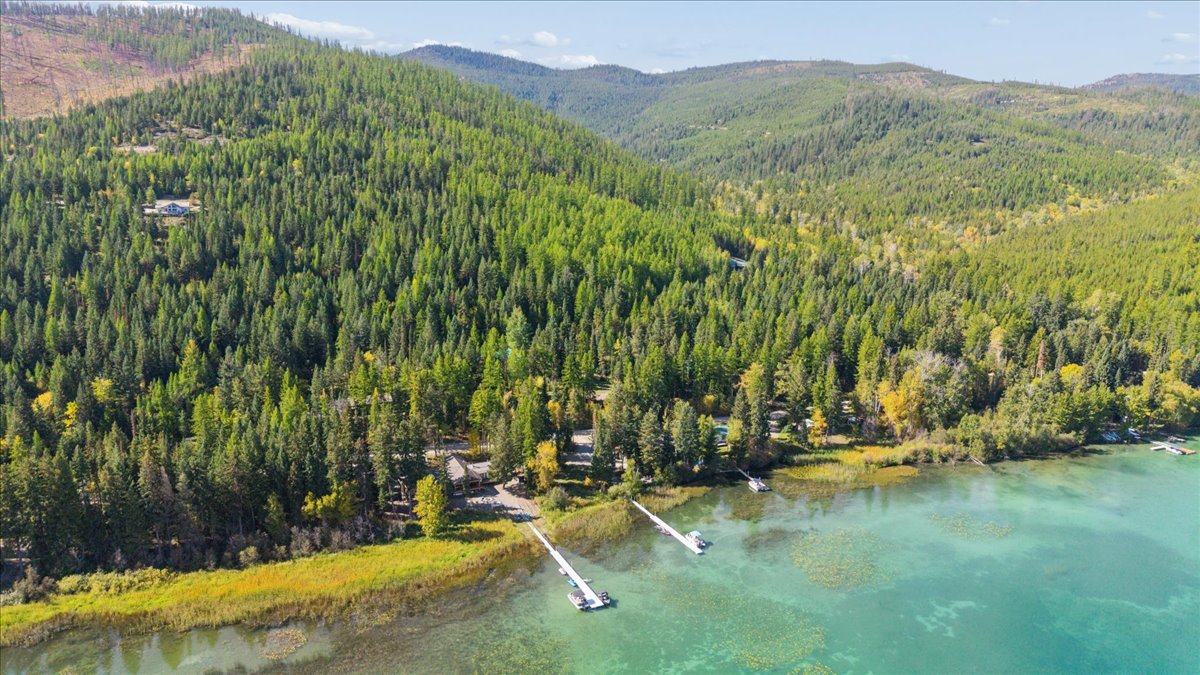 Aerial view of a forested lakeshore property with several docks extending into clear turquoise water.