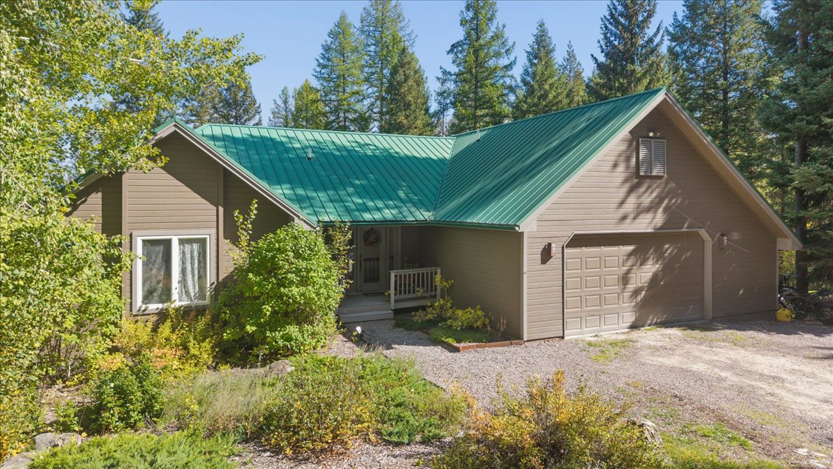 Brown home with a green metal roof, attached garage, and covered entry among trees.