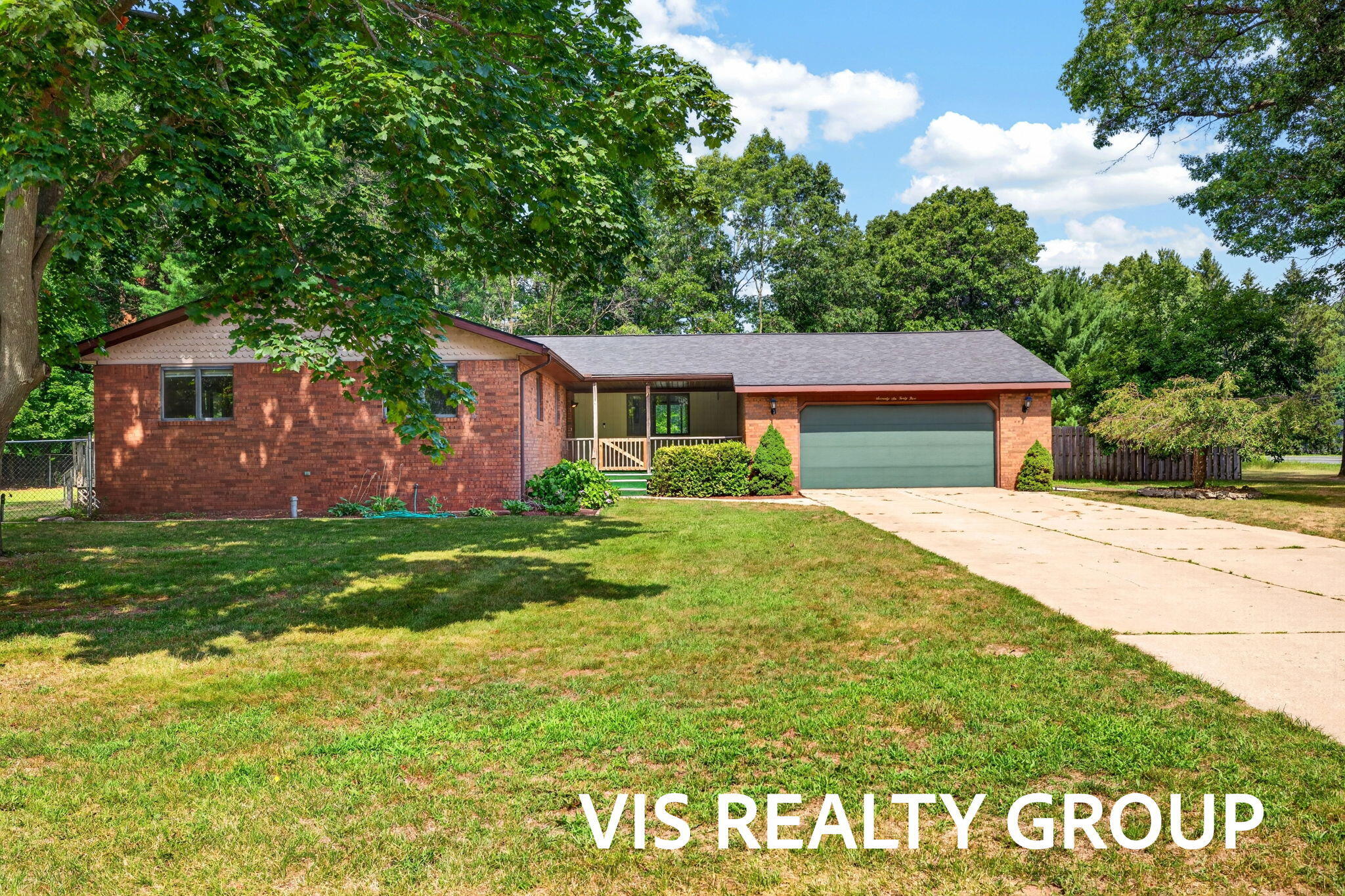 Red brick ranch house with an attached garage, covered porch, and mature trees.