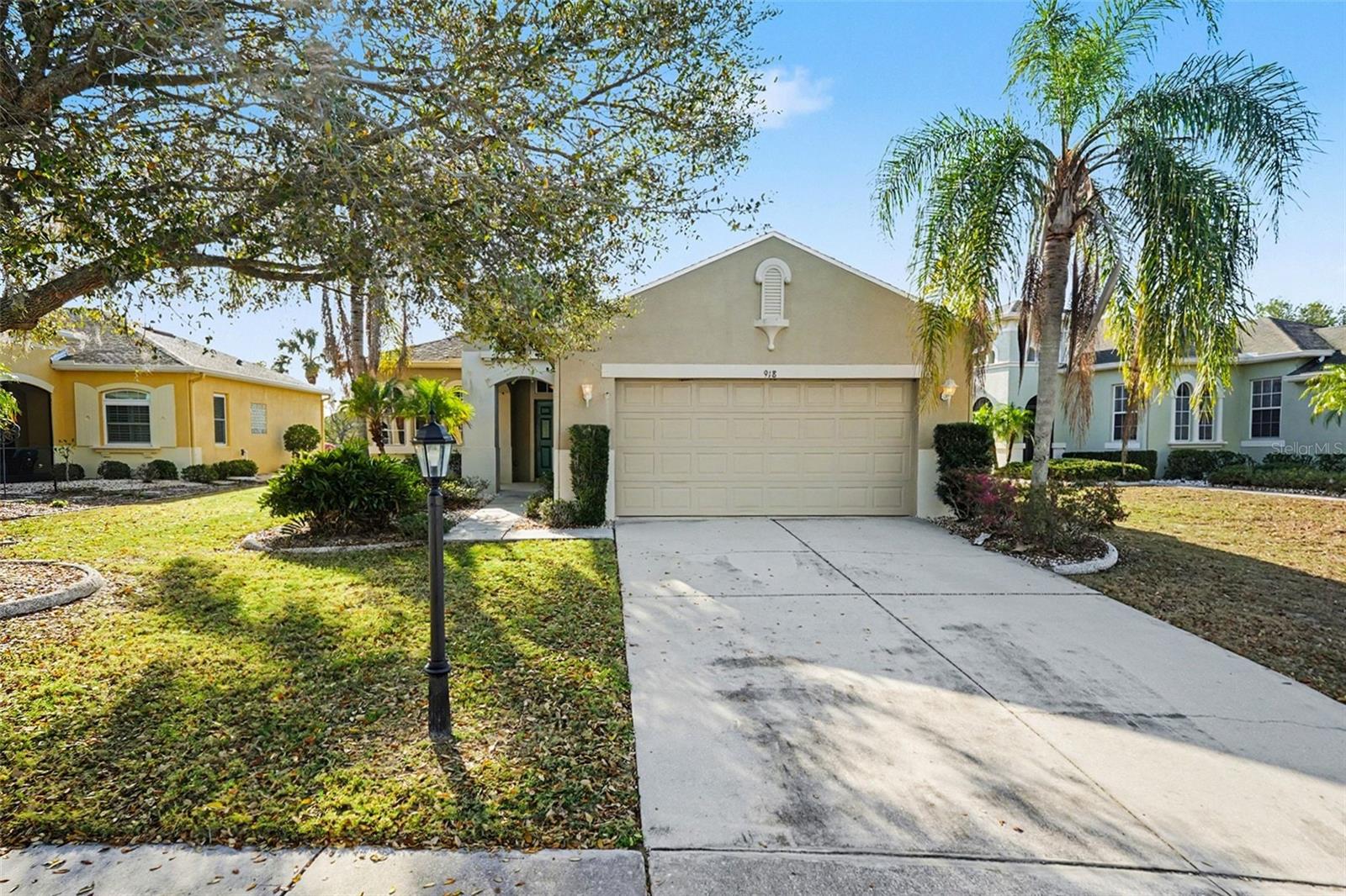 Single-story beige home with a two-car garage, concrete driveway, and palm trees in the front yard.