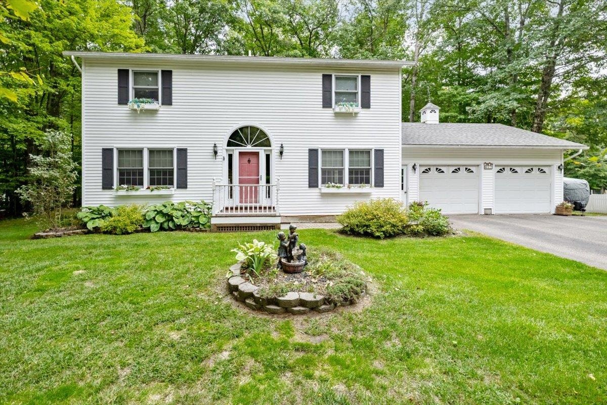 White two-story home with a red front door, attached two-car garage, and leafy wooded surroundings.