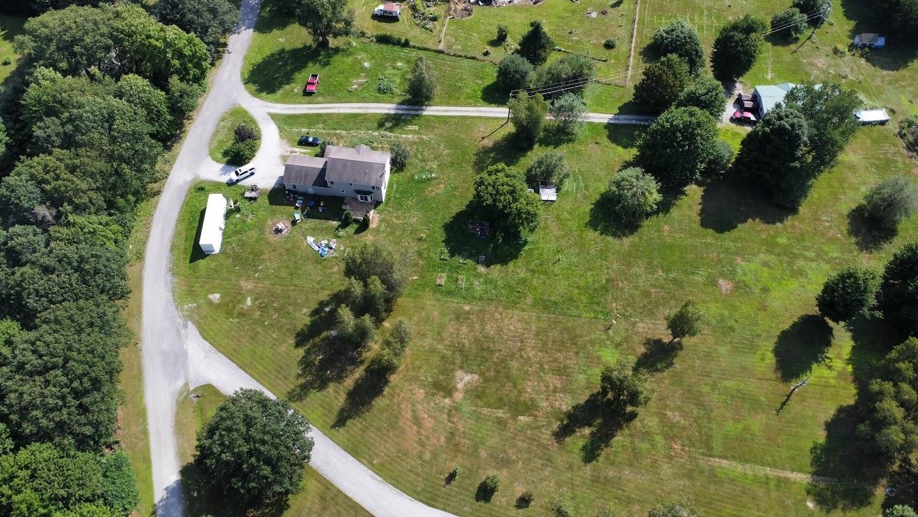 Aerial view of a detached house on a large grassy lot beside a gravel road.