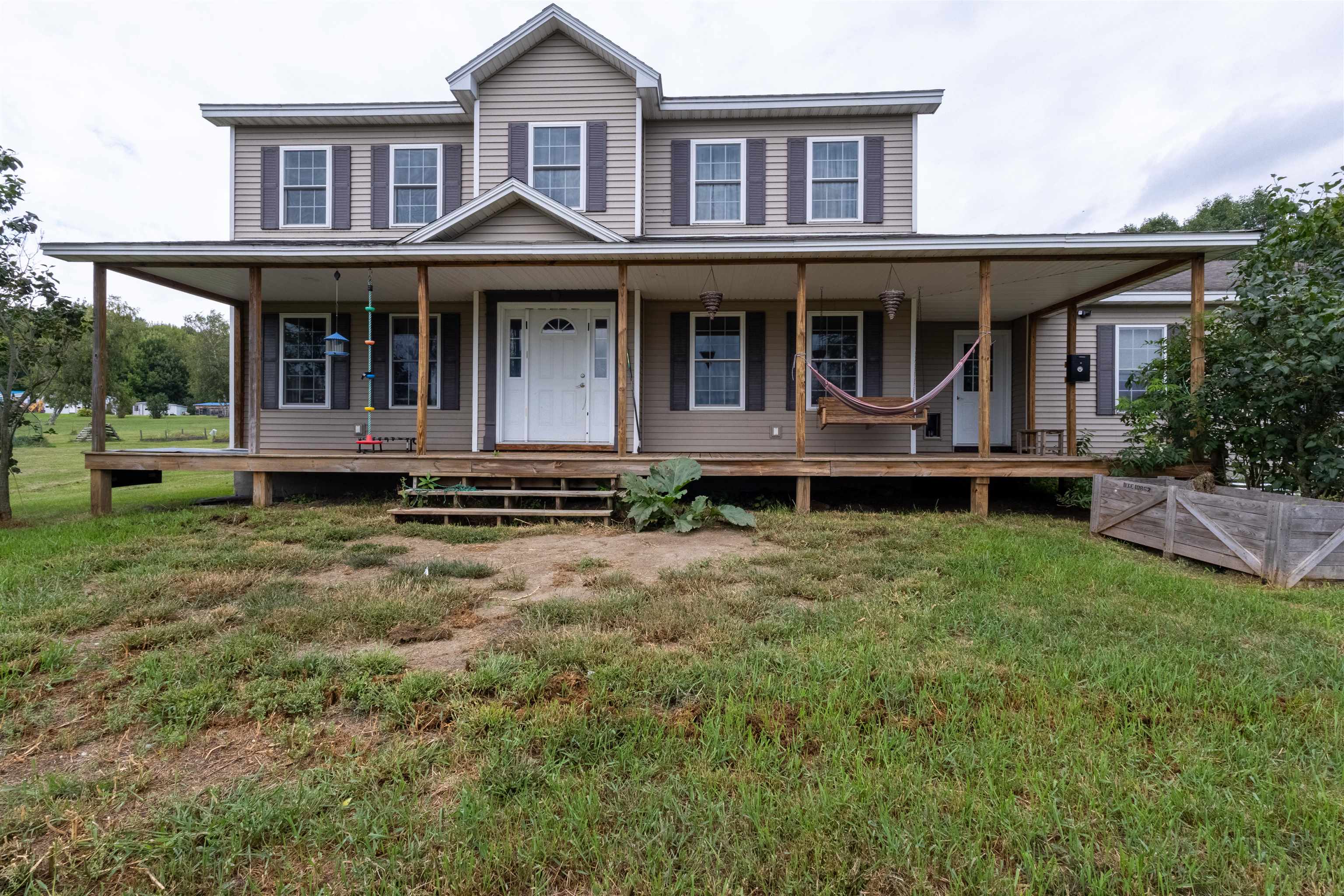 Two-story beige house with a wide covered porch, hammock, and grassy front yard.