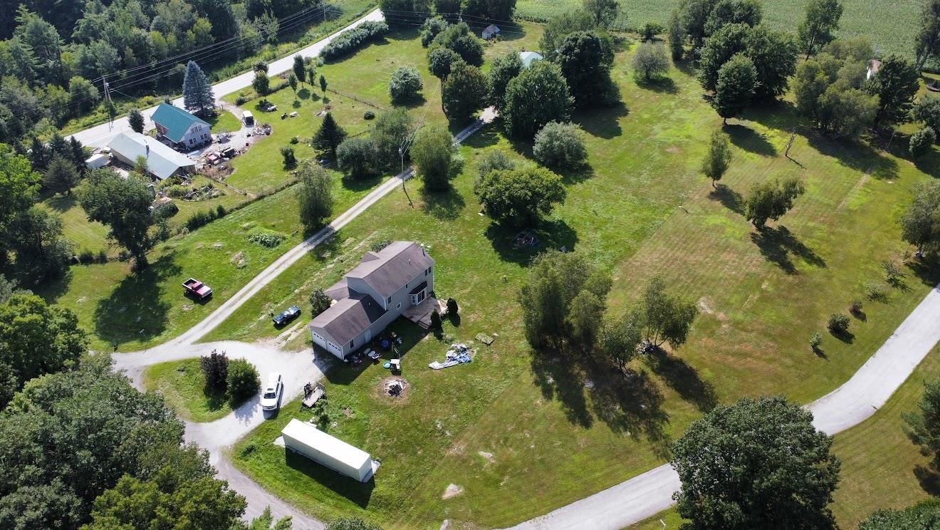 Aerial view of a rural home with a curved driveway, detached outbuilding, and expansive grassy grounds.