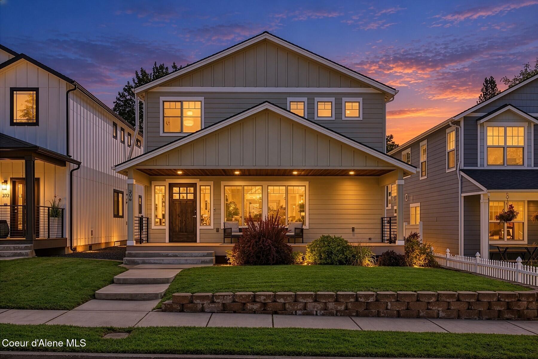 Two-story gray house with a covered porch and warmly lit windows at dusk.