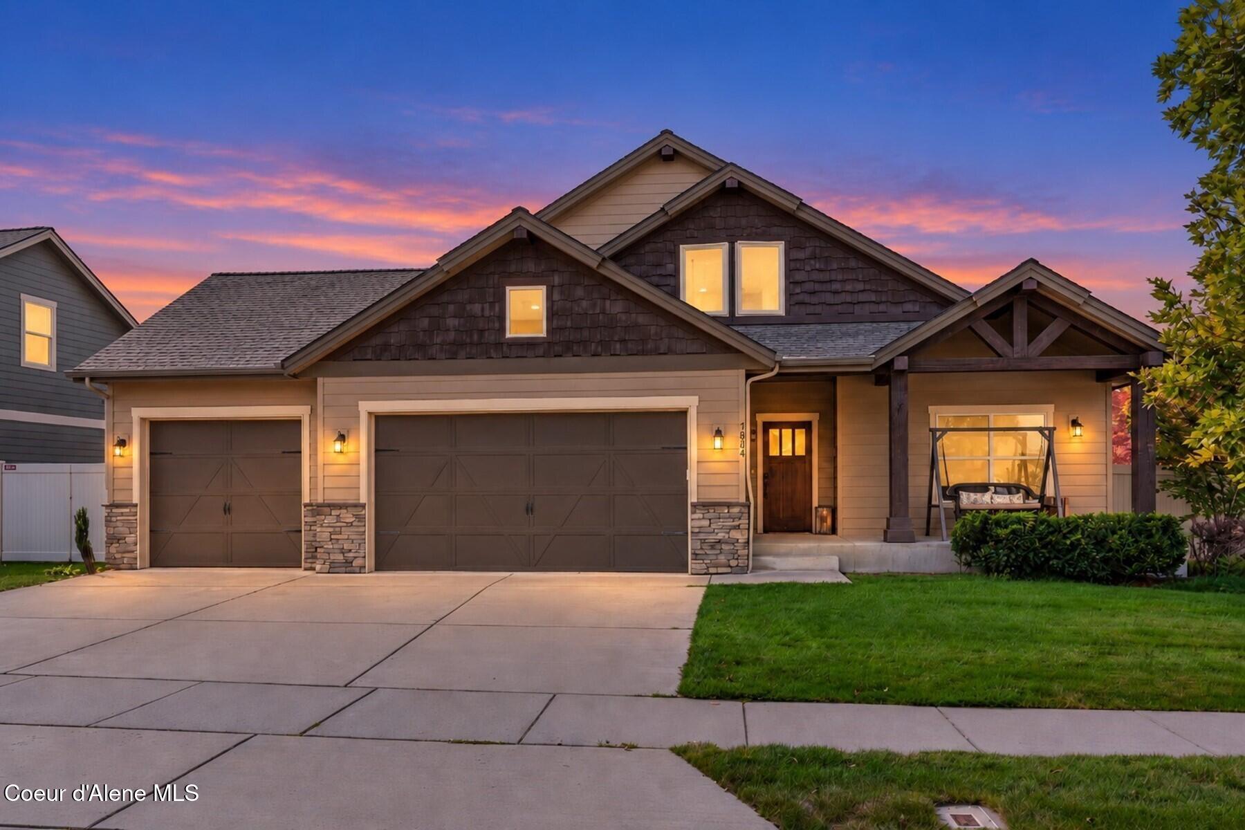 Two-story house at dusk with twin garages, a covered porch swing, and glowing windows.