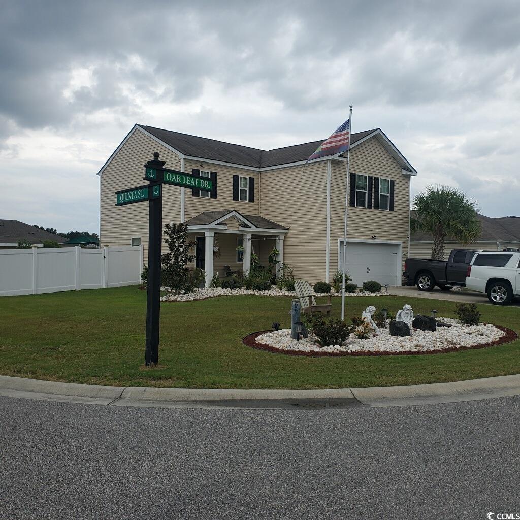 Two-story beige house with an attached garage, covered porch, American flag, and landscaped front yard.