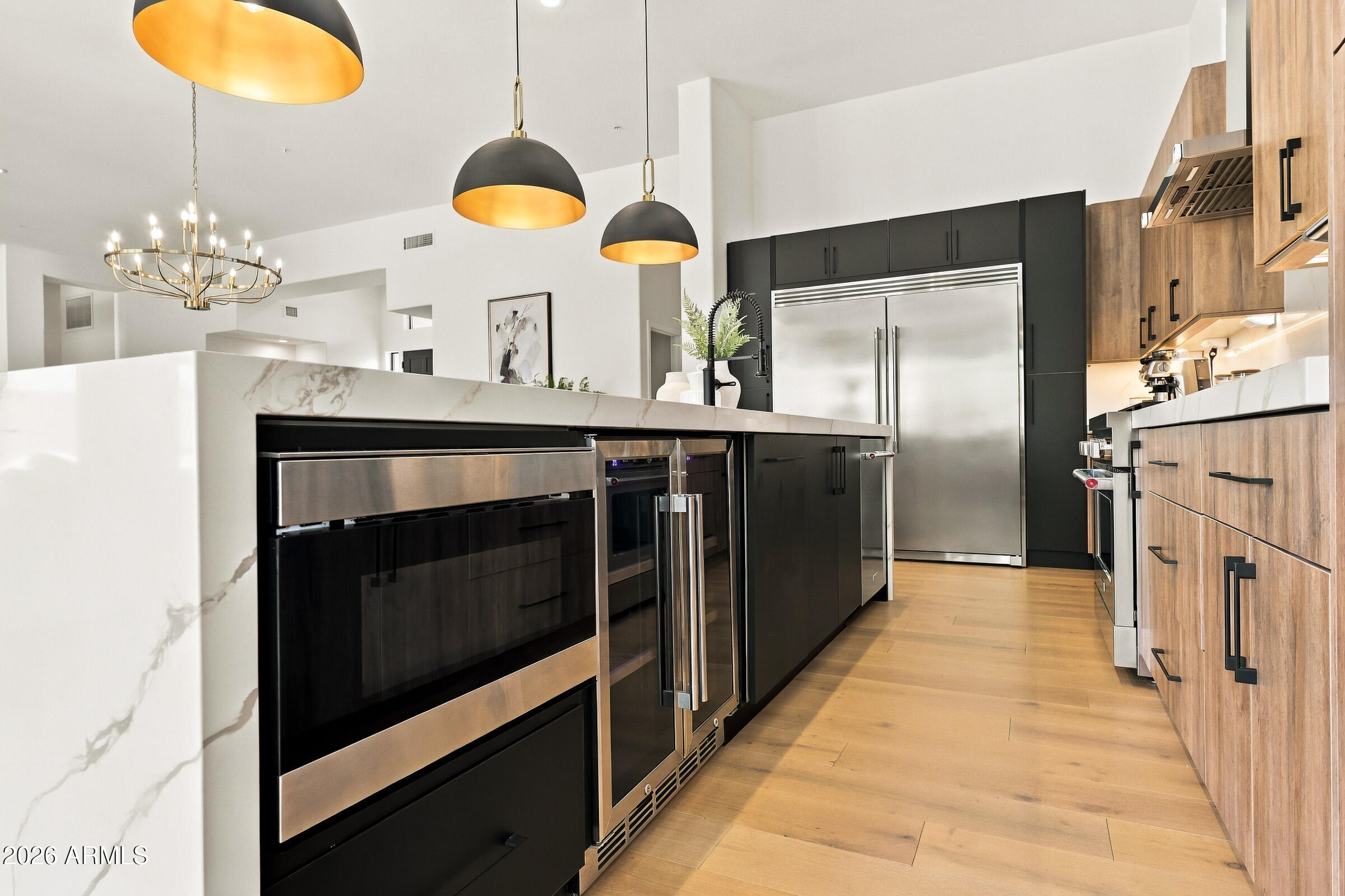 Modern kitchen with a marble island, dark cabinetry, stainless steel appliances, and wood flooring.