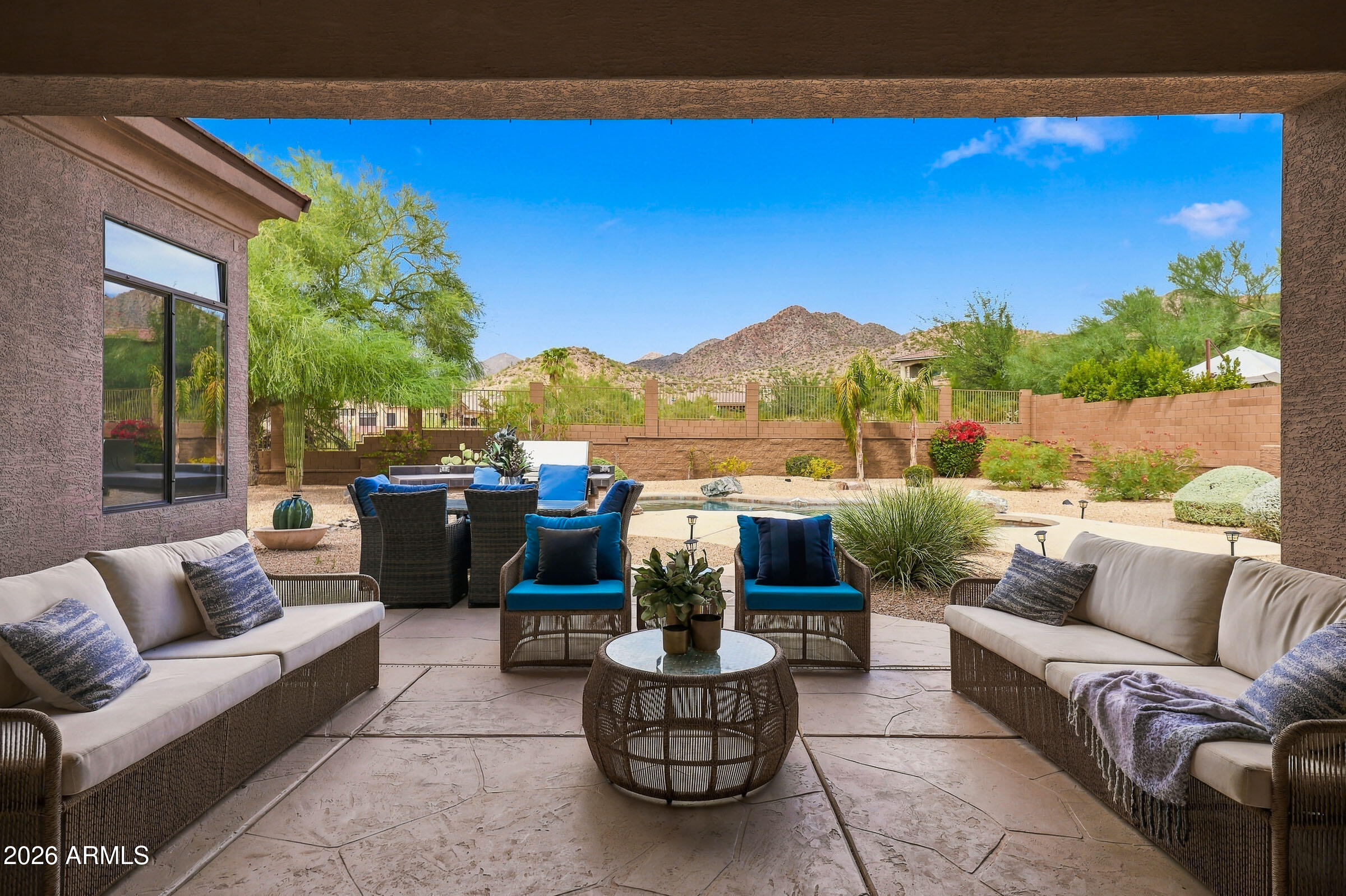 Covered patio with wicker seating overlooking a backyard pool and desert mountains.