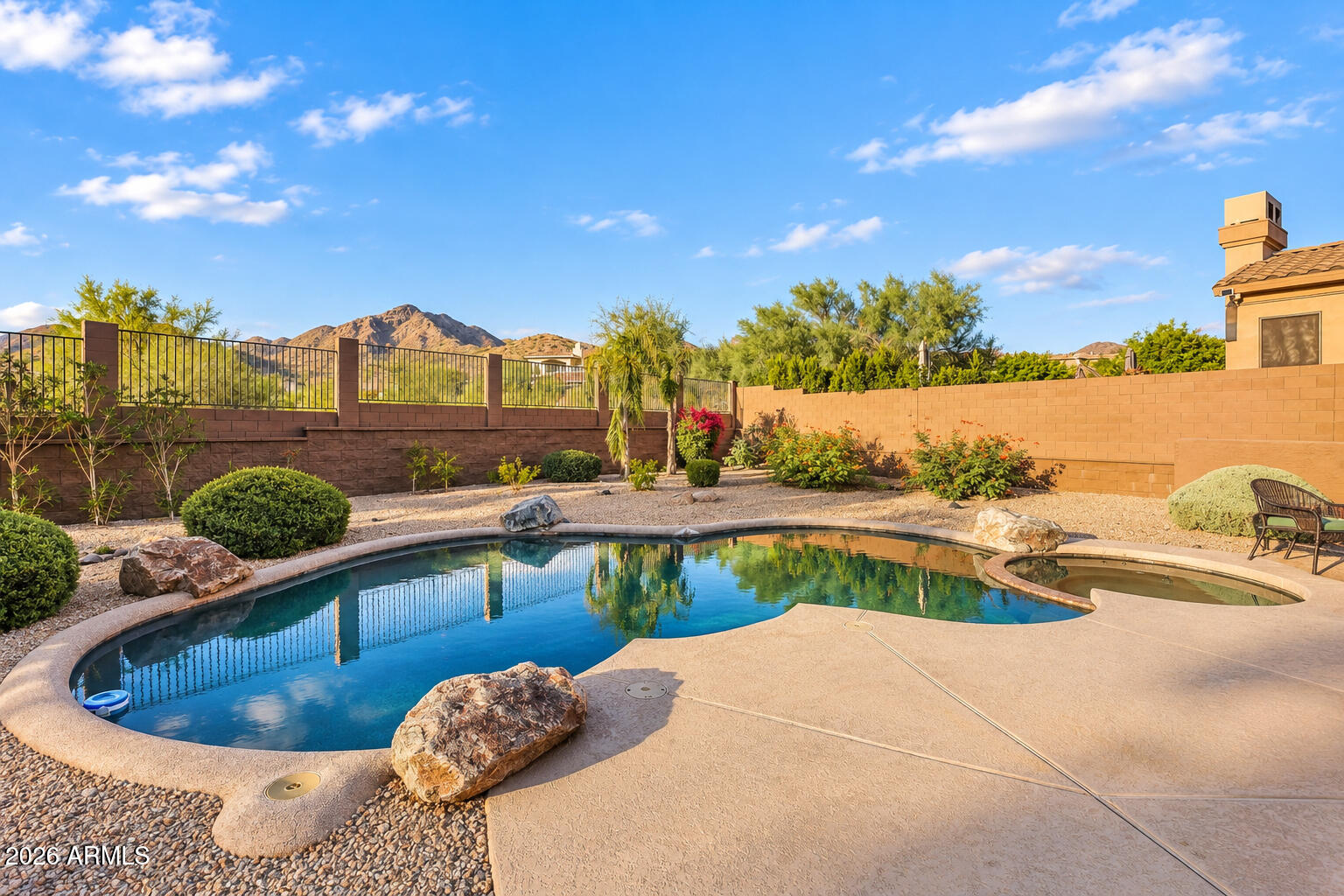 Backyard pool and spa beside a broad patio, with desert landscaping and mountains beyond the wall.