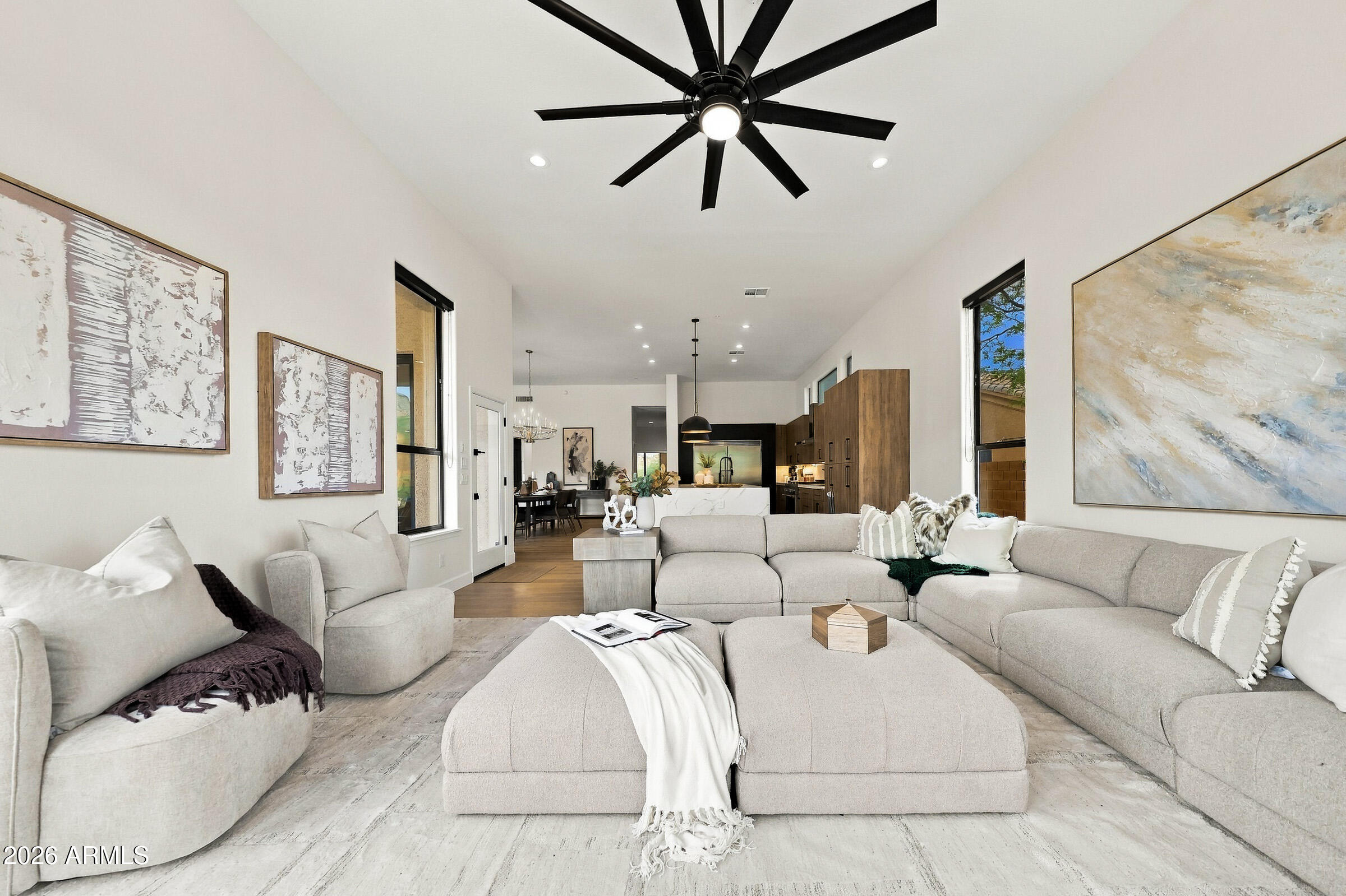 Furnished living room with a large sectional, oversized black ceiling fan, and open-plan kitchen beyond.