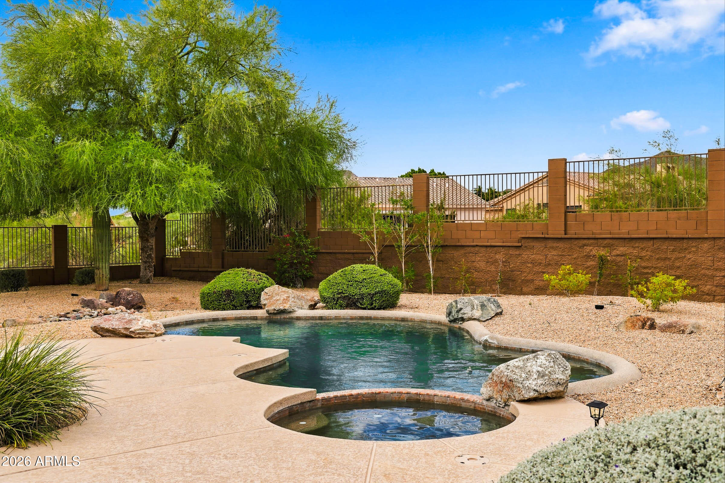 Backyard pool and circular spa beside a concrete deck, desert landscaping, and mature shade trees.
