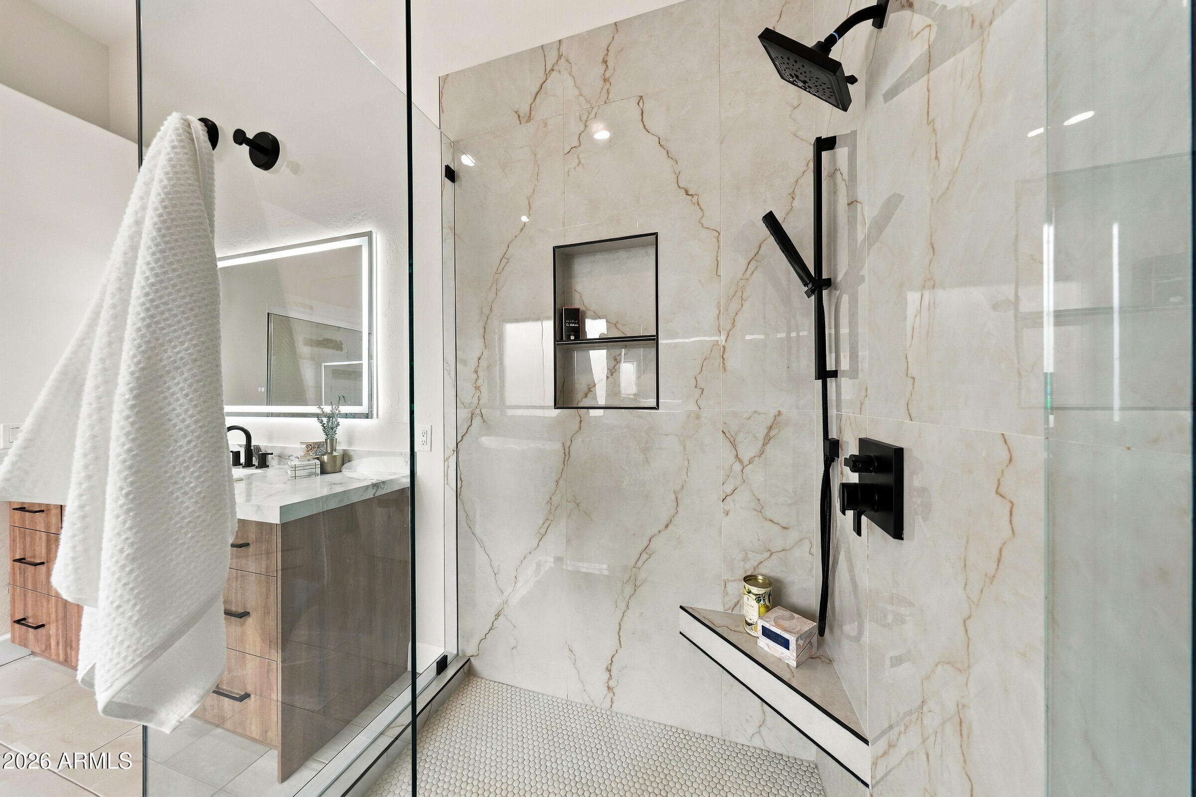 Walk-in shower with veined tile, matte black fixtures, and a glass enclosure beside a wood vanity.