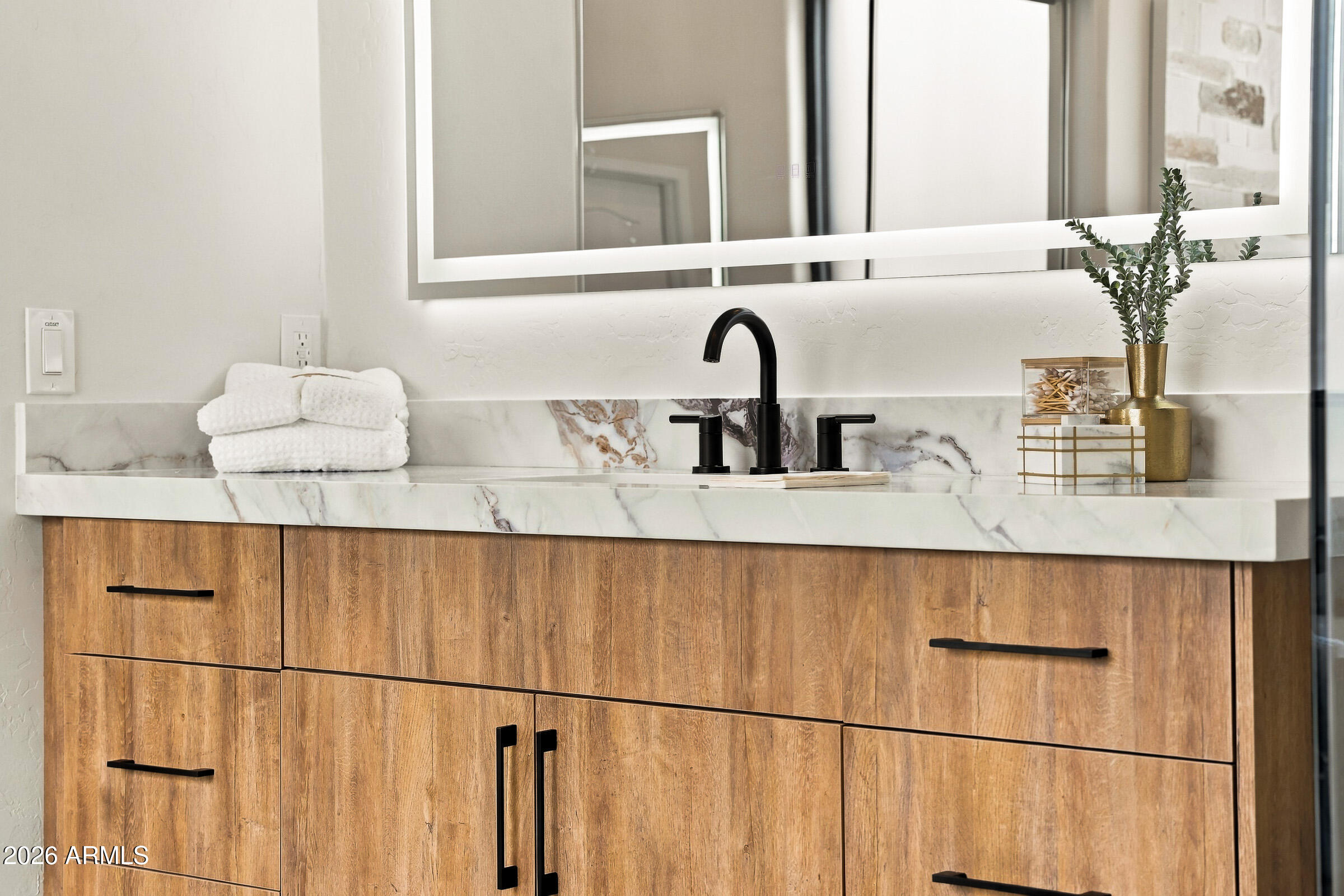 Bathroom vanity with warm wood cabinets, marble countertop, and black faucet.