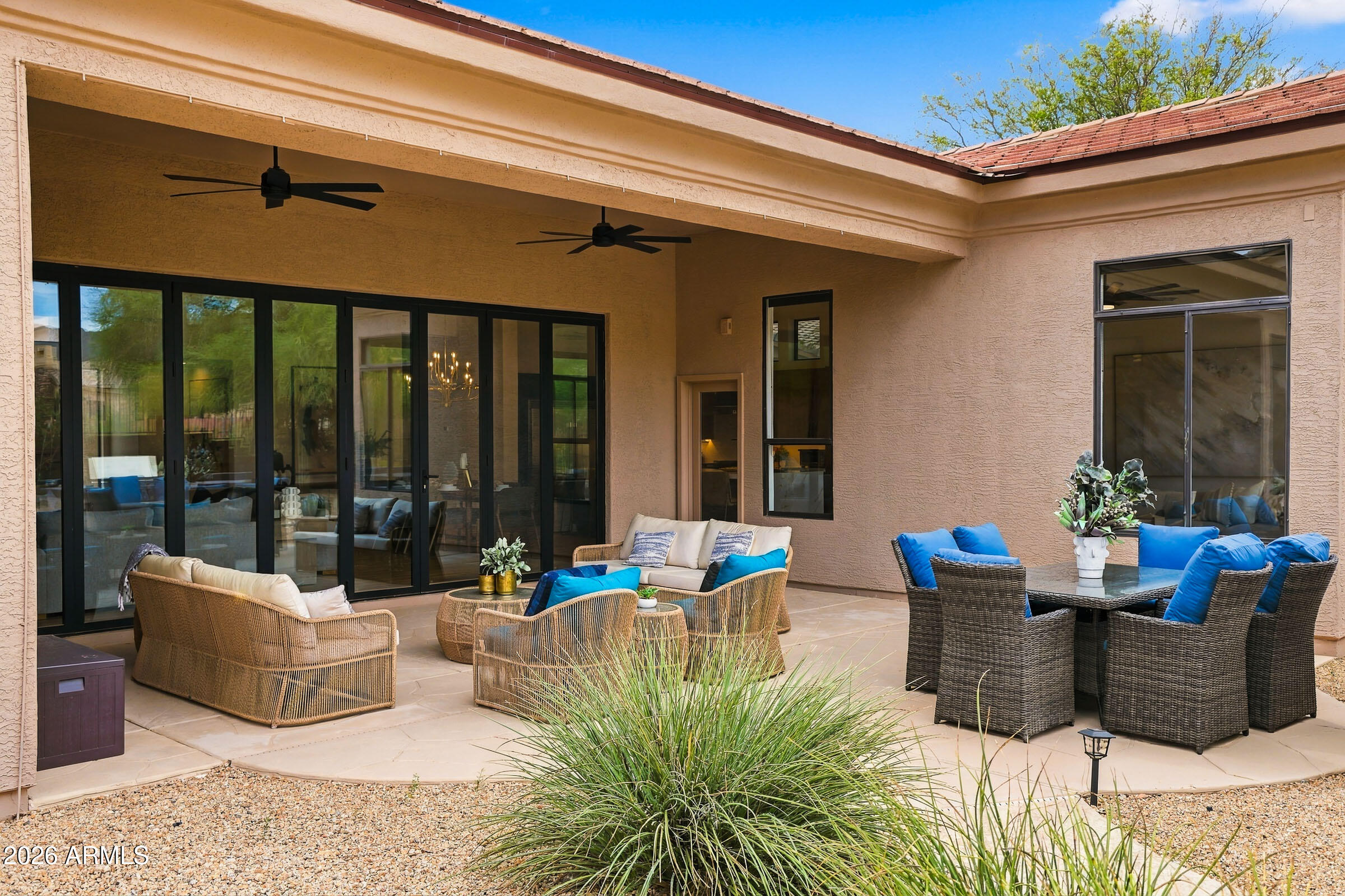 Covered patio with wicker lounge seating, blue-cushioned dining chairs, and black-framed sliding glass doors.
