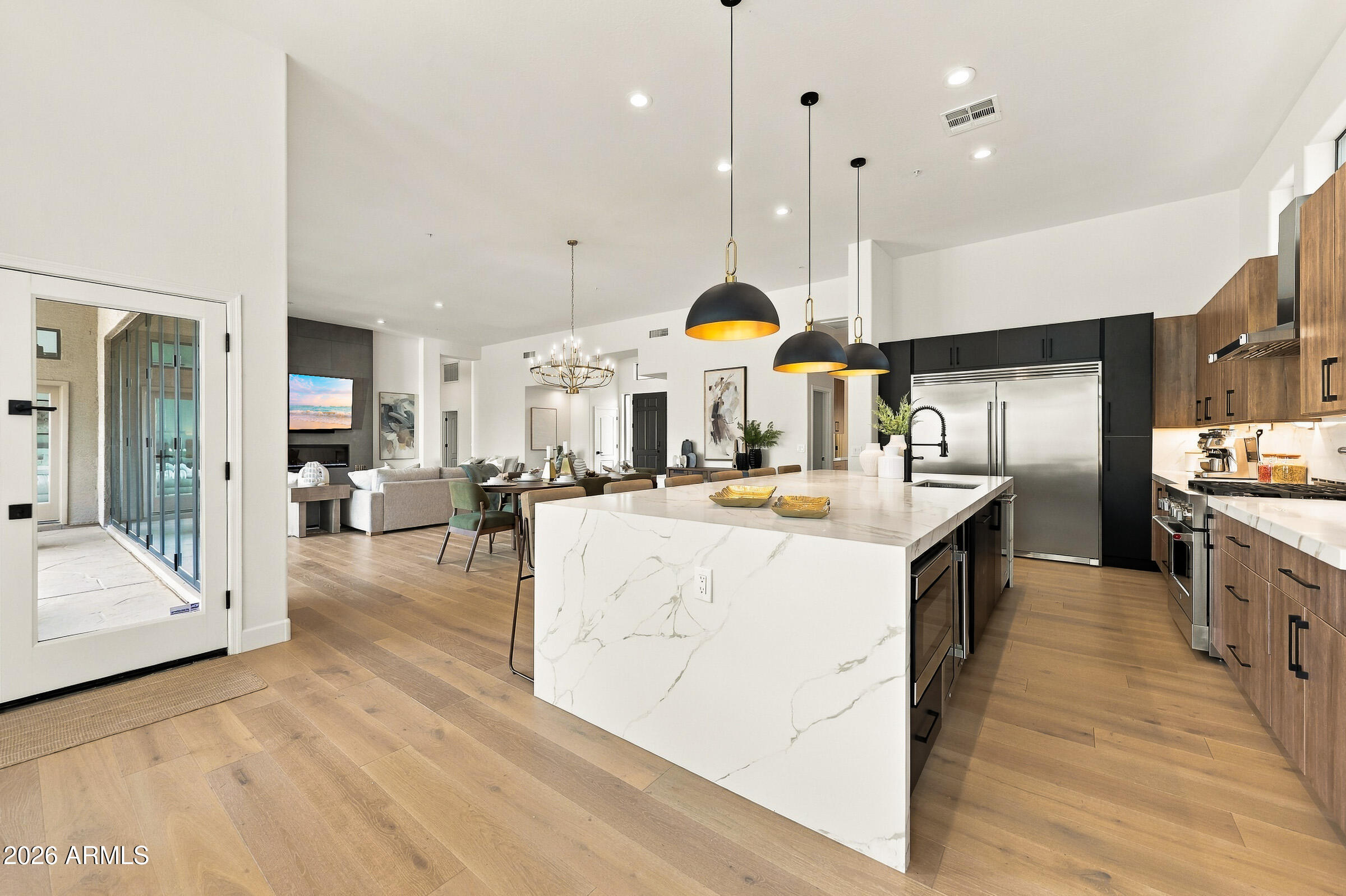 Open kitchen with a veined-stone island, warm wood cabinetry, and living area beyond.