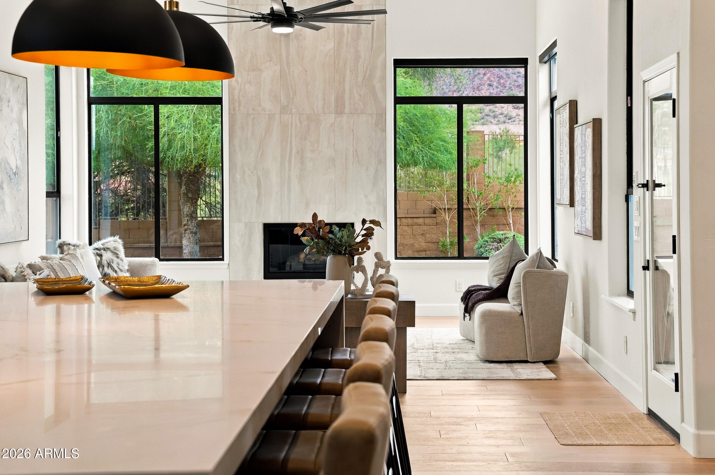 Open-plan kitchen and living area with a stone island, fireplace, and tall garden-facing windows.