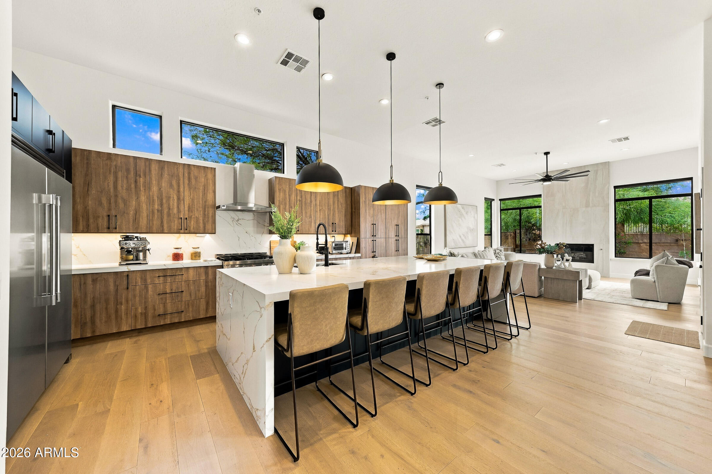 Modern kitchen with a marble island, wood cabinetry, and an open living room beyond.