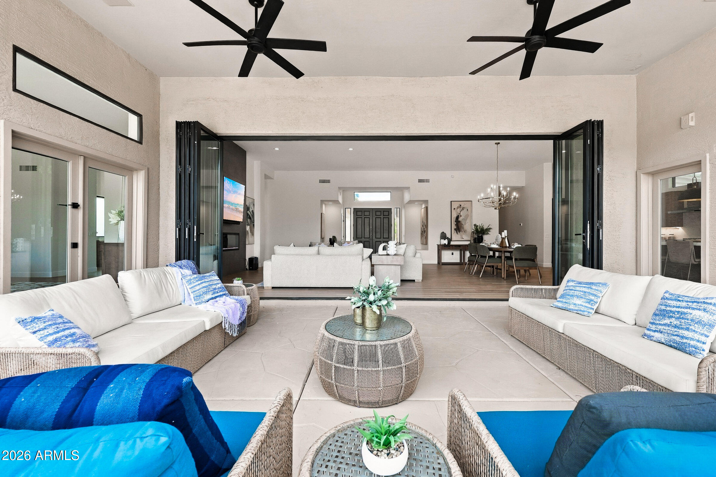 Covered patio seating with blue cushions opens through folding glass doors to the living and dining area.