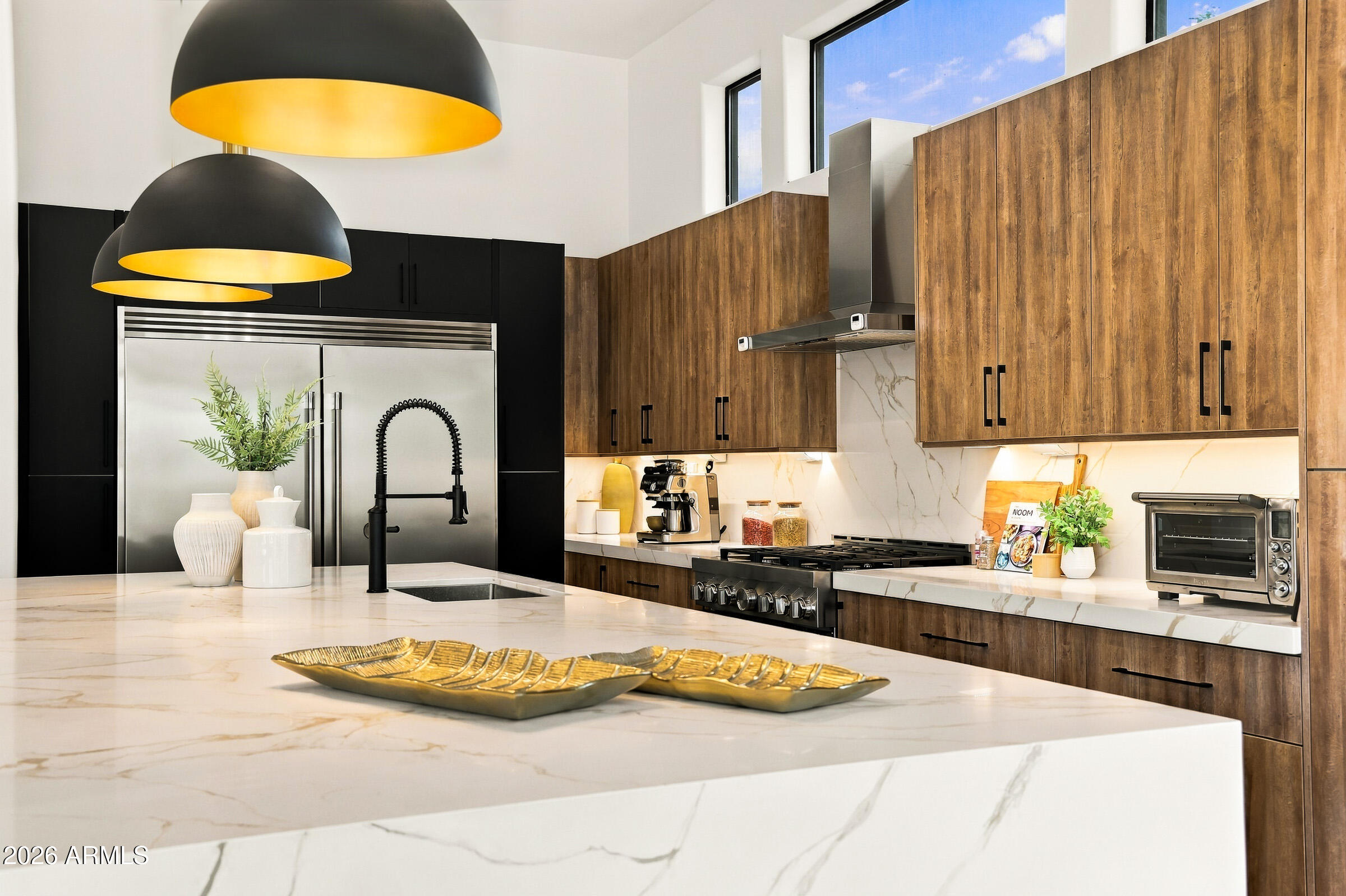 Modern kitchen with a marble island, wood cabinetry, and oversized black-and-gold pendant lights.