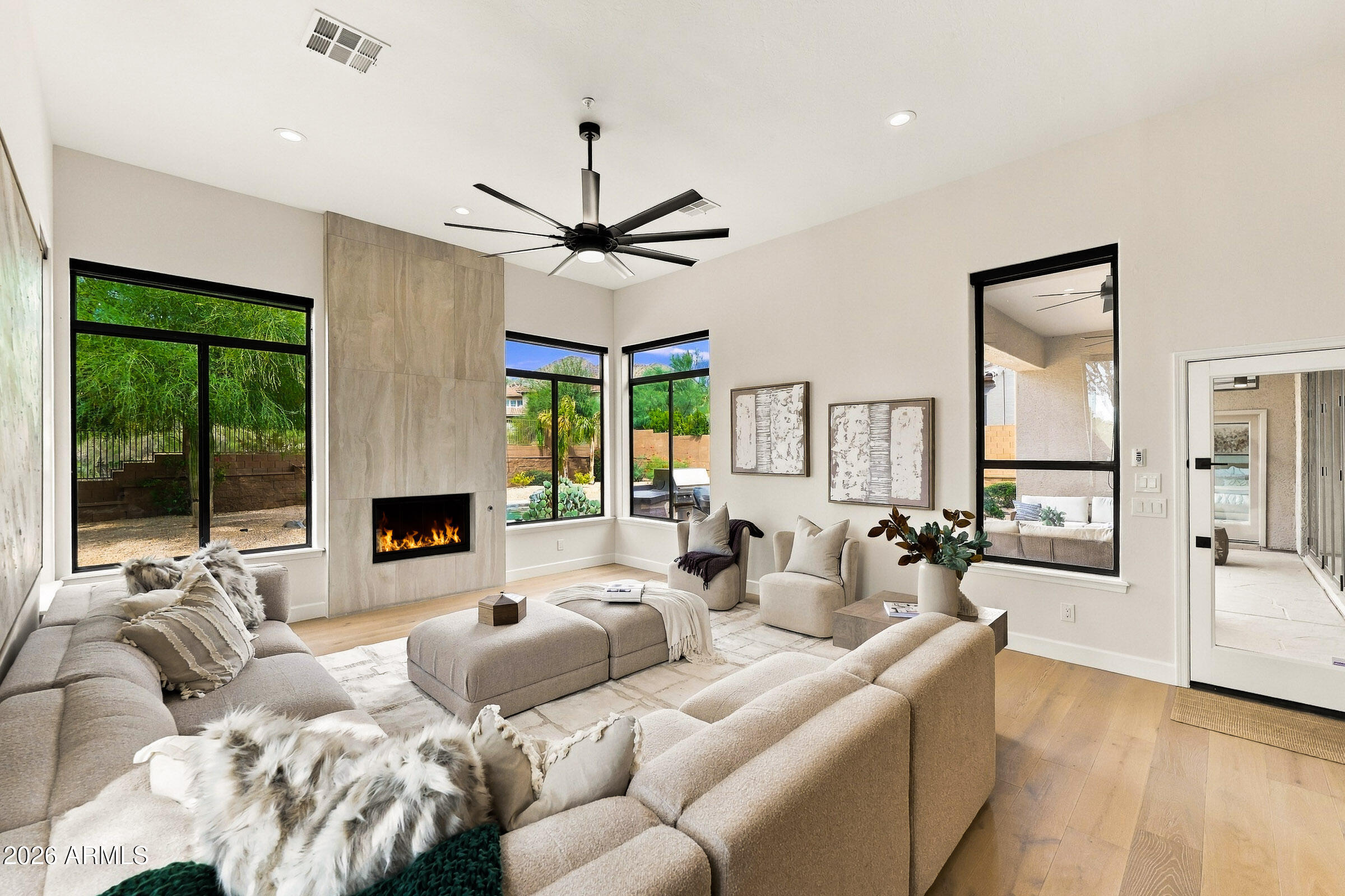 Living room with a tiled fireplace, large black-framed windows, and neutral furnishings.