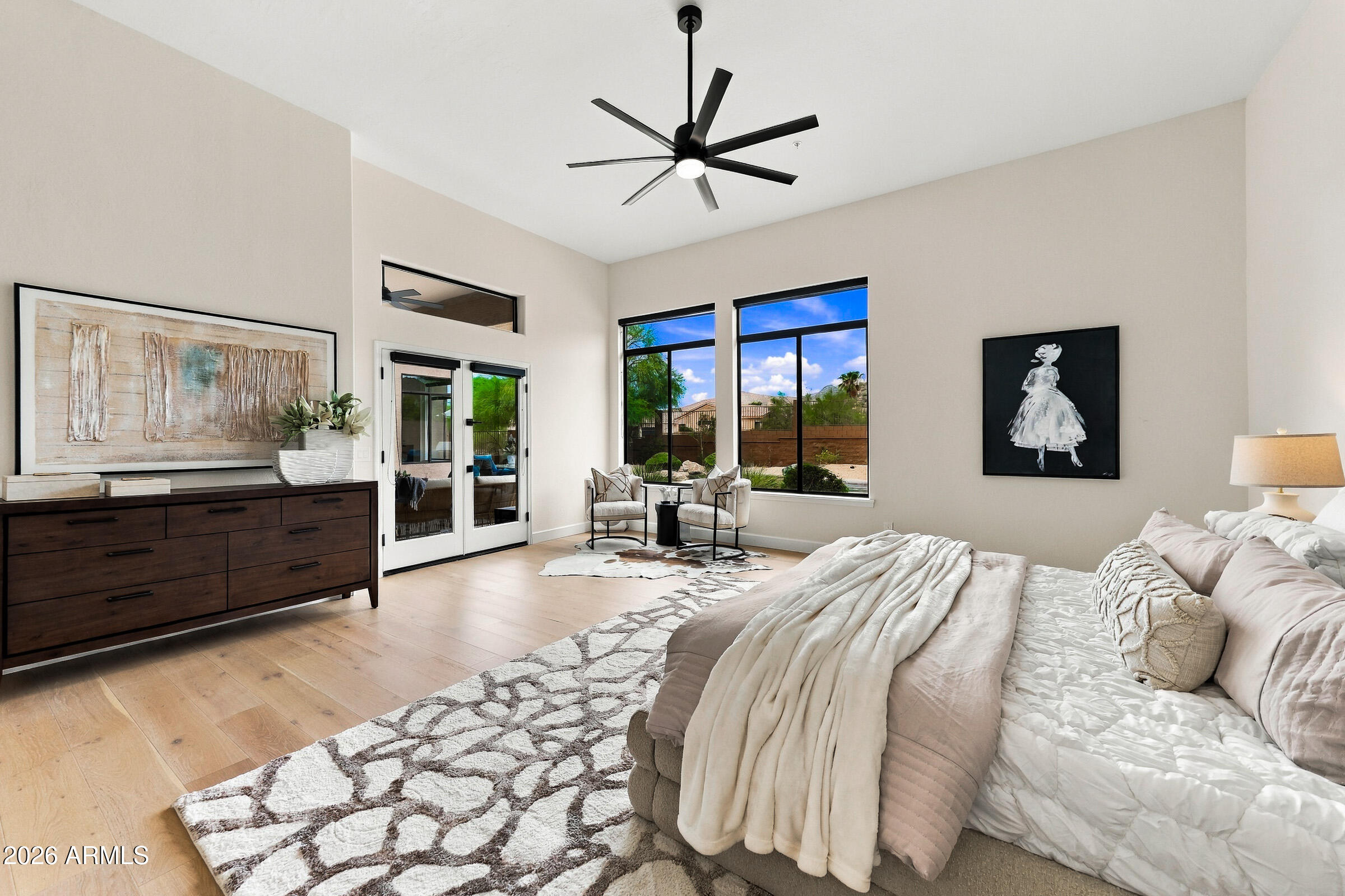 Bright bedroom with a large bed, tall windows, and a sitting area.