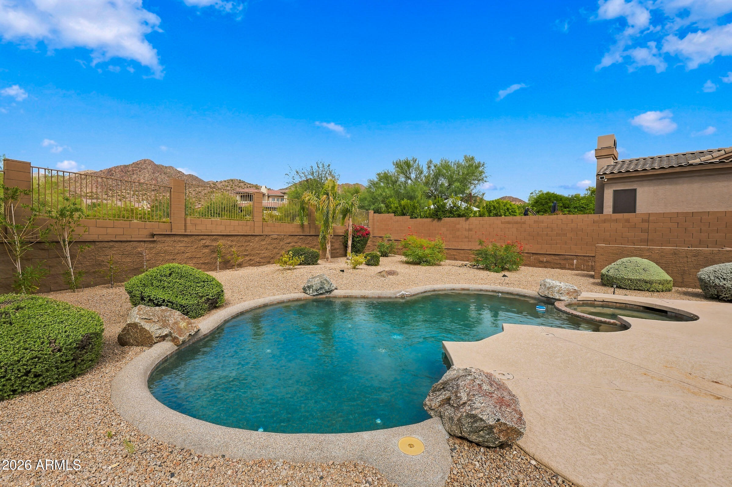 Backyard swimming pool and raised spa bordered by desert landscaping, with mountains beyond the wall.
