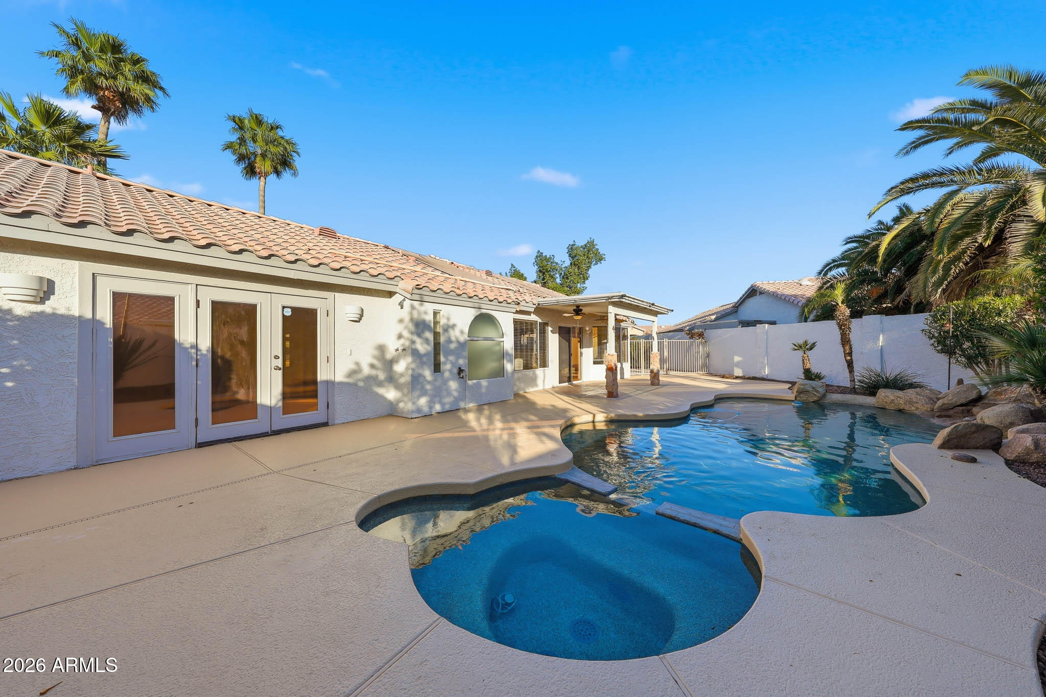 Backyard pool beside a stucco home, with a broad deck, palm trees, and covered patio.