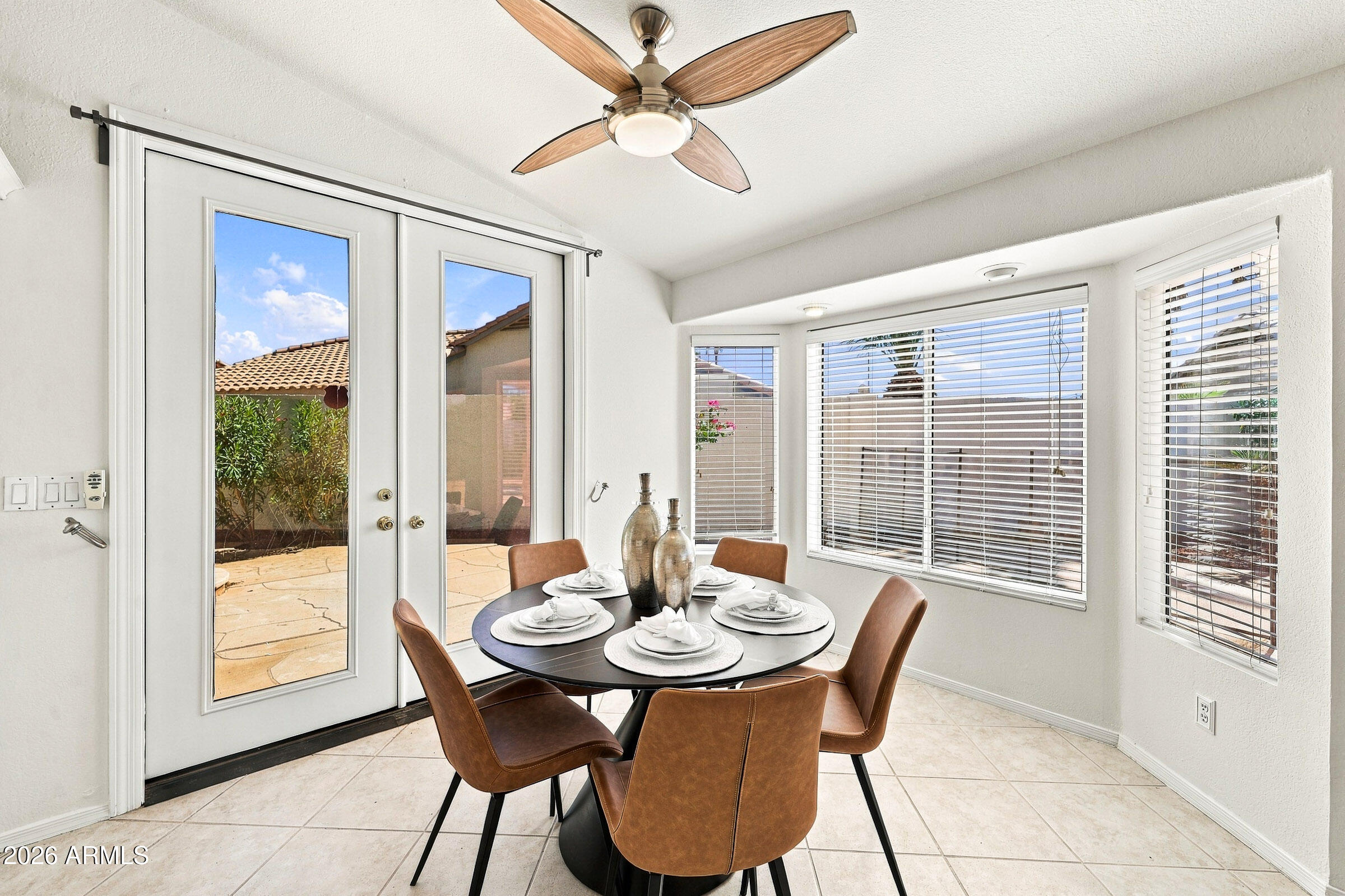 Dining nook with a round set table, four brown chairs, and glass doors opening to a paved patio.