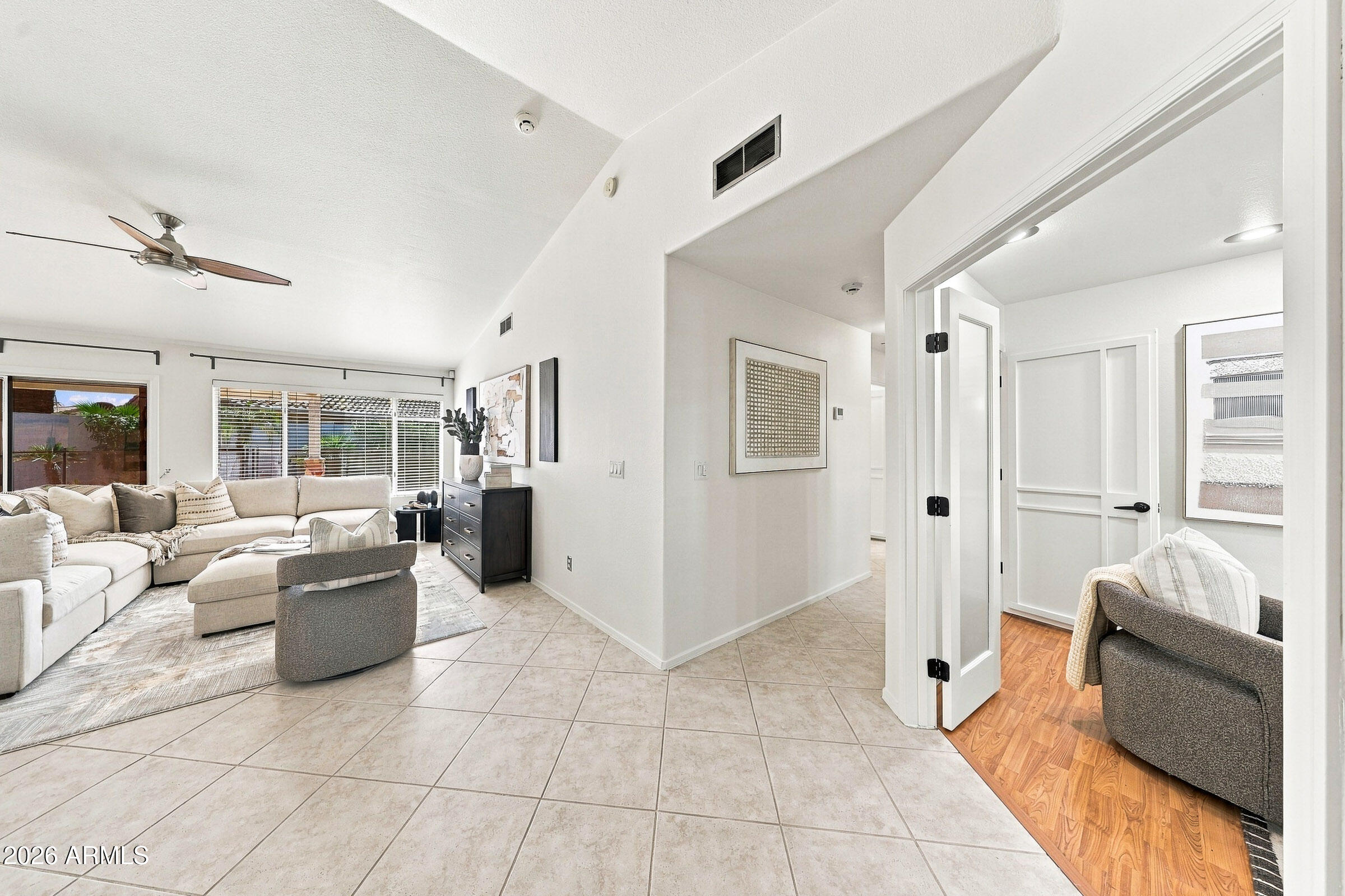 Living room with a large sectional, vaulted ceiling, pale tile floors, and an adjoining sitting area.