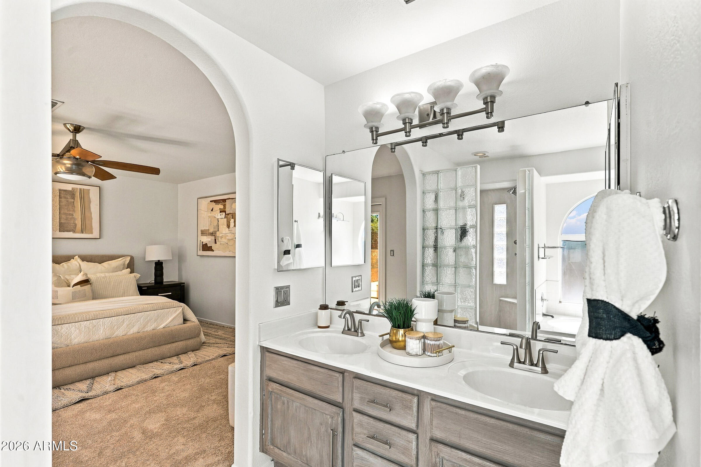 Primary bathroom with a double vanity and glass-block shower wall, opening onto a bedroom.