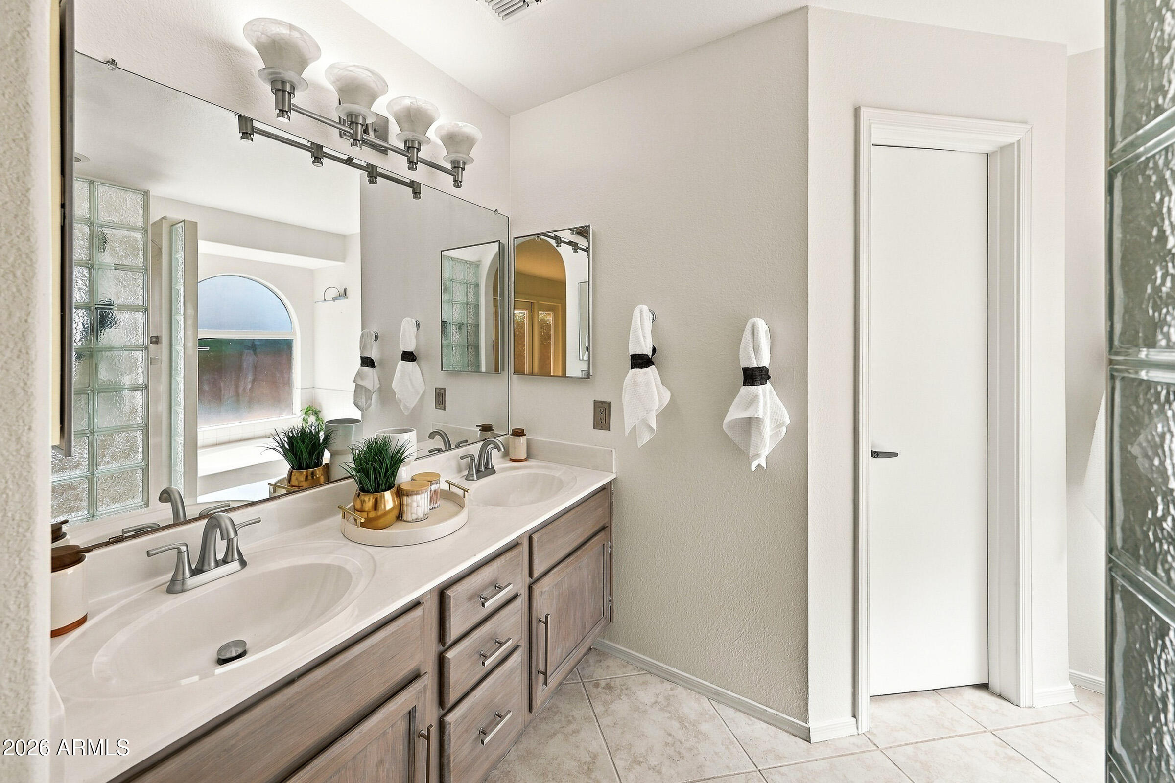 Bathroom with a double-sink vanity, glass-block walls, and an arched frosted window.