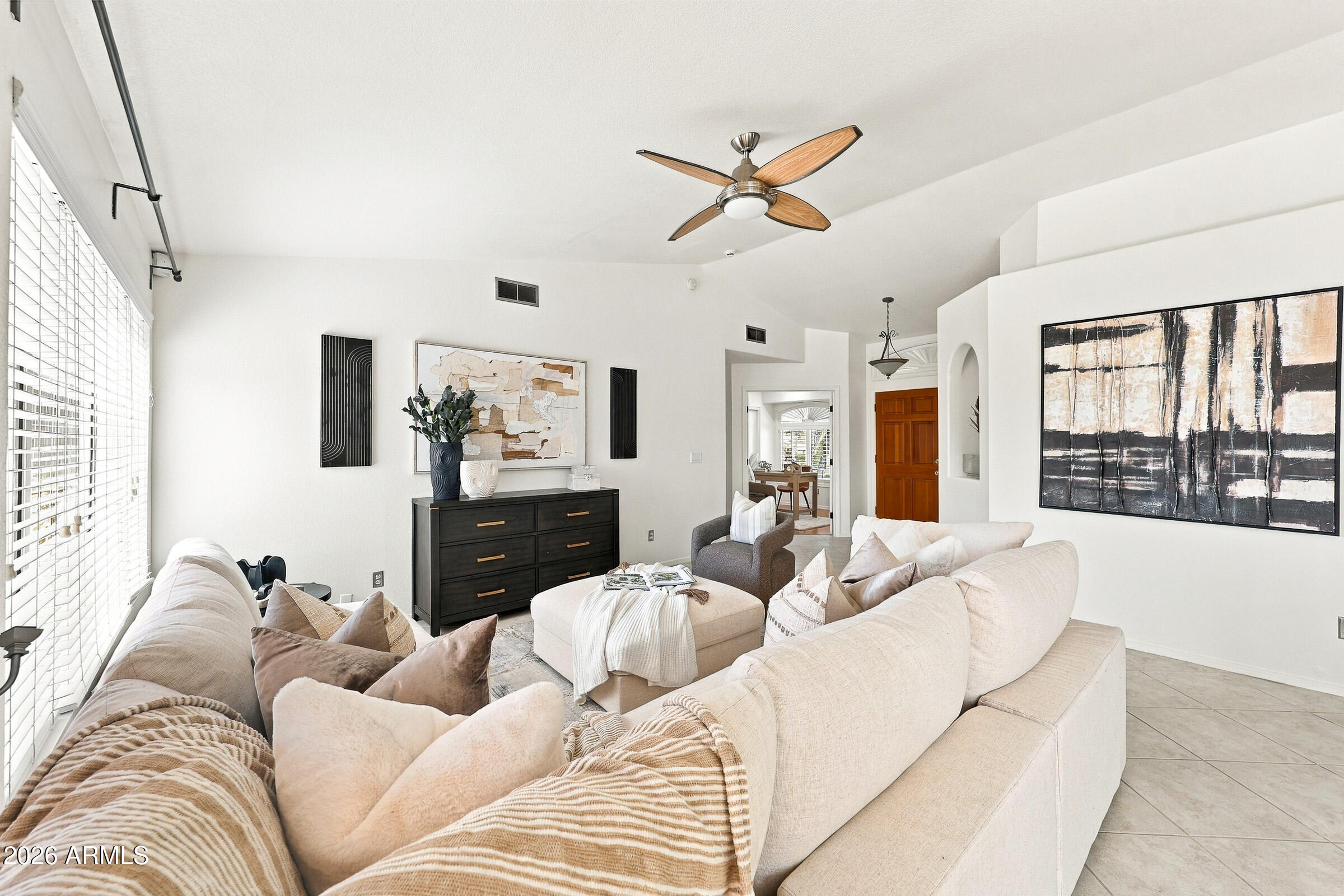 Furnished living room with cream sofas, a wood-blade ceiling fan, and large shuttered windows.
