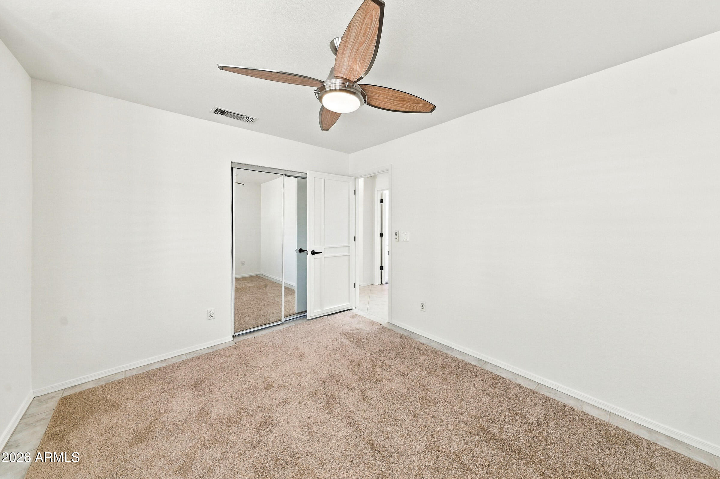 Empty carpeted bedroom with mirrored closet doors and a wood-blade ceiling fan.