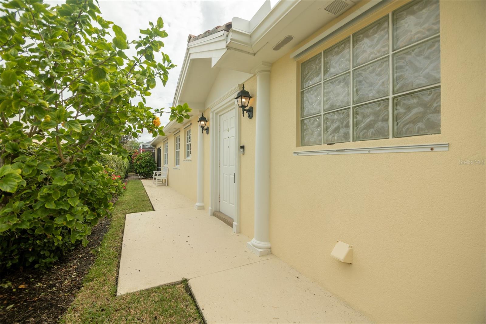 Pale yellow home exterior with a columned entry, glass-block window, and landscaped walkway.