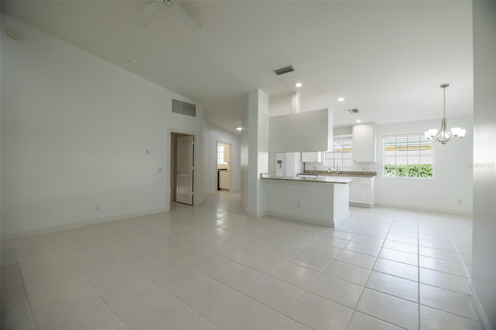 Open-plan kitchen and dining area with a granite breakfast bar, white cabinets, and tiled floors.