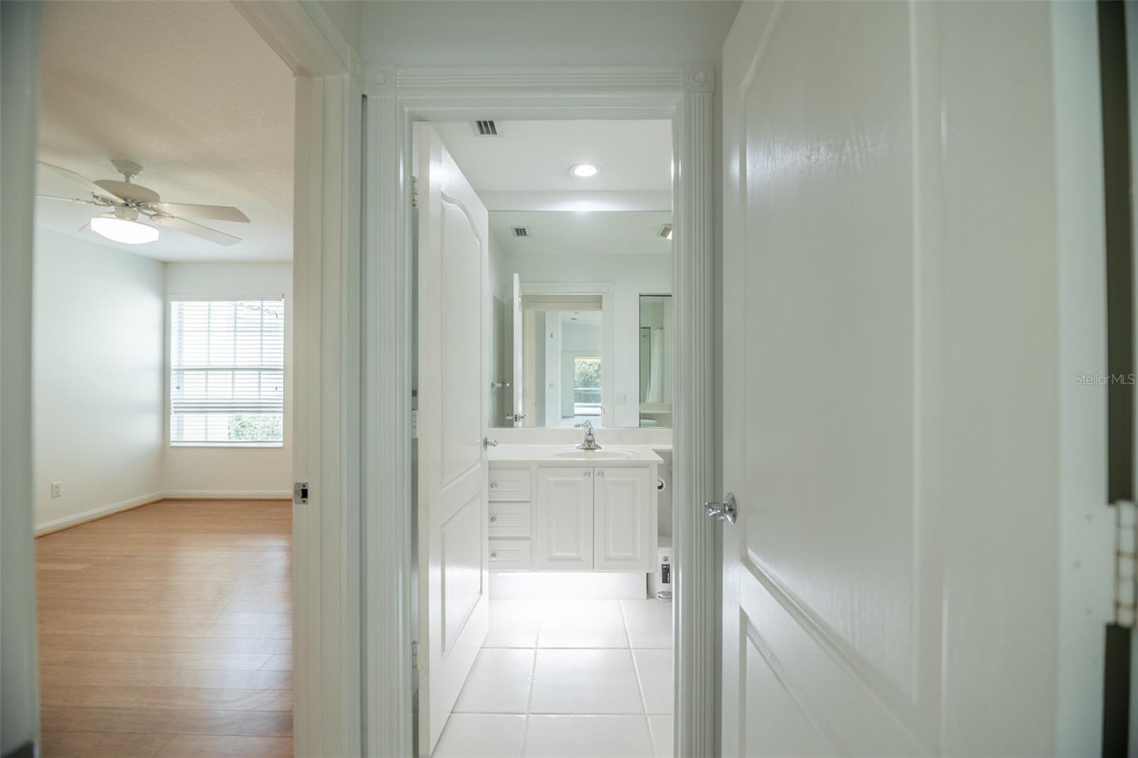 Bathroom with white vanity and tiled floor, viewed through a doorway beside an empty room.