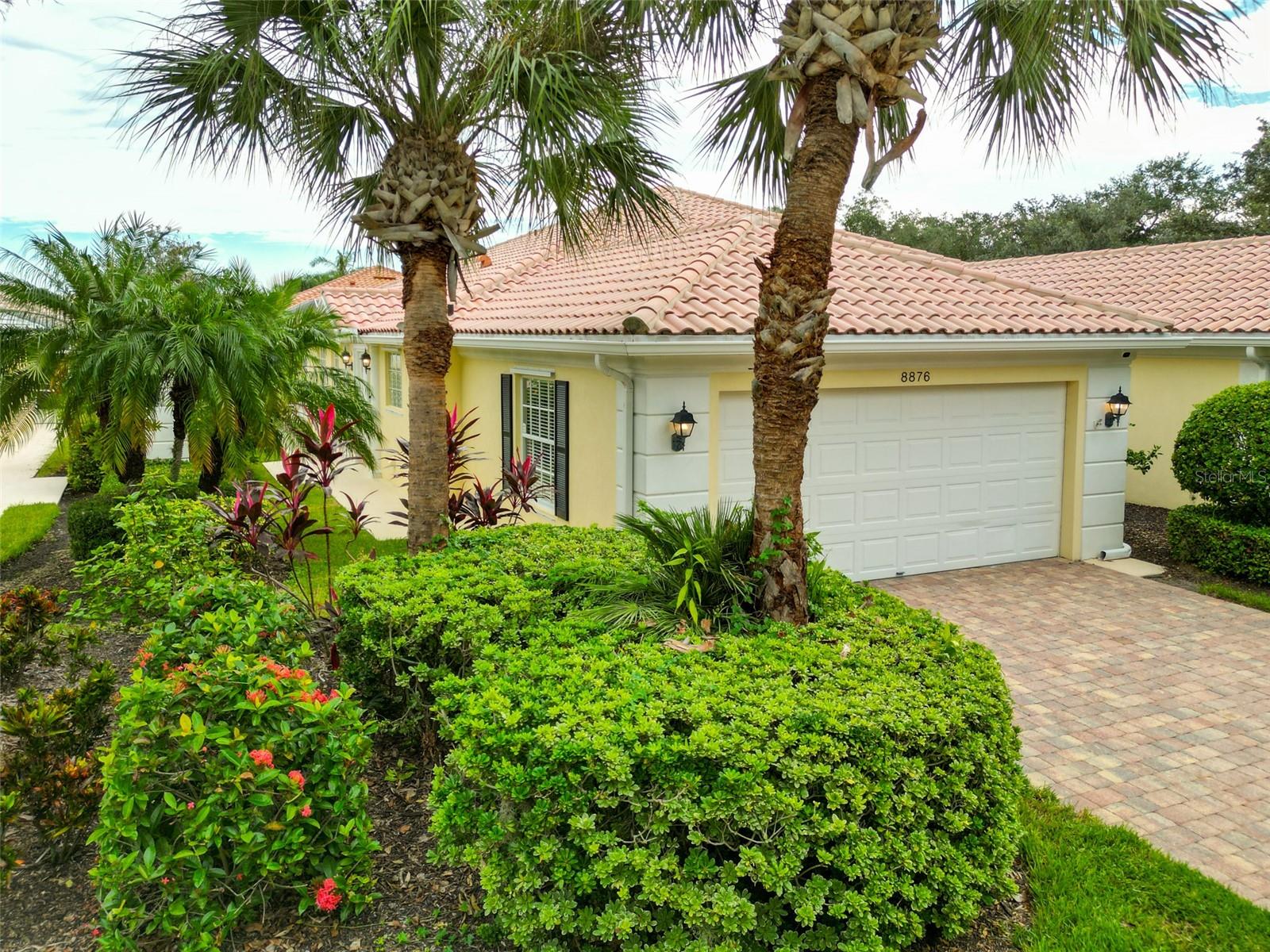 Yellow stucco home with tile roof, palms, landscaped entry, and paver driveway.