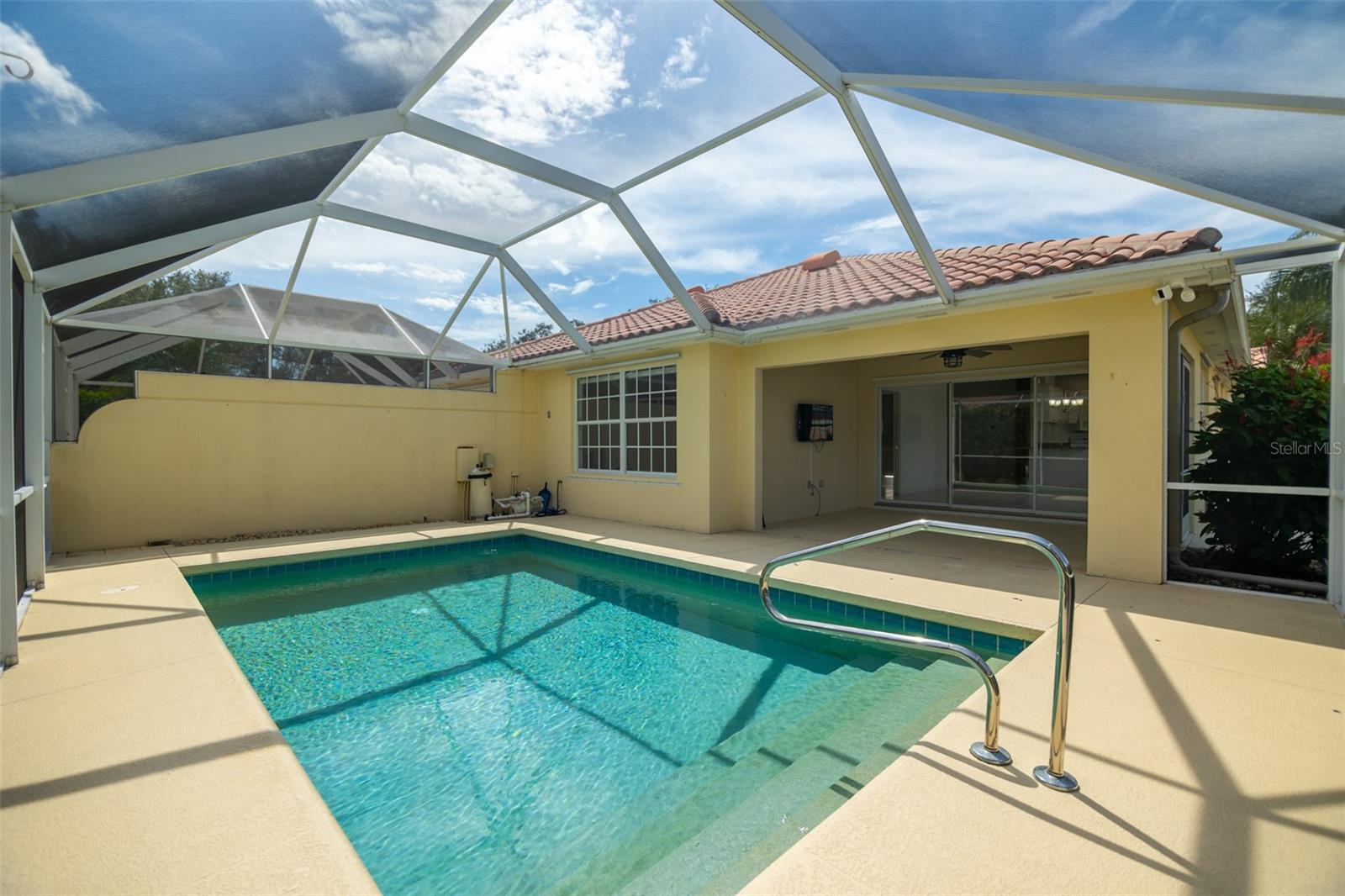 Backyard pool beneath a screened enclosure, with a covered patio and yellow stucco home.