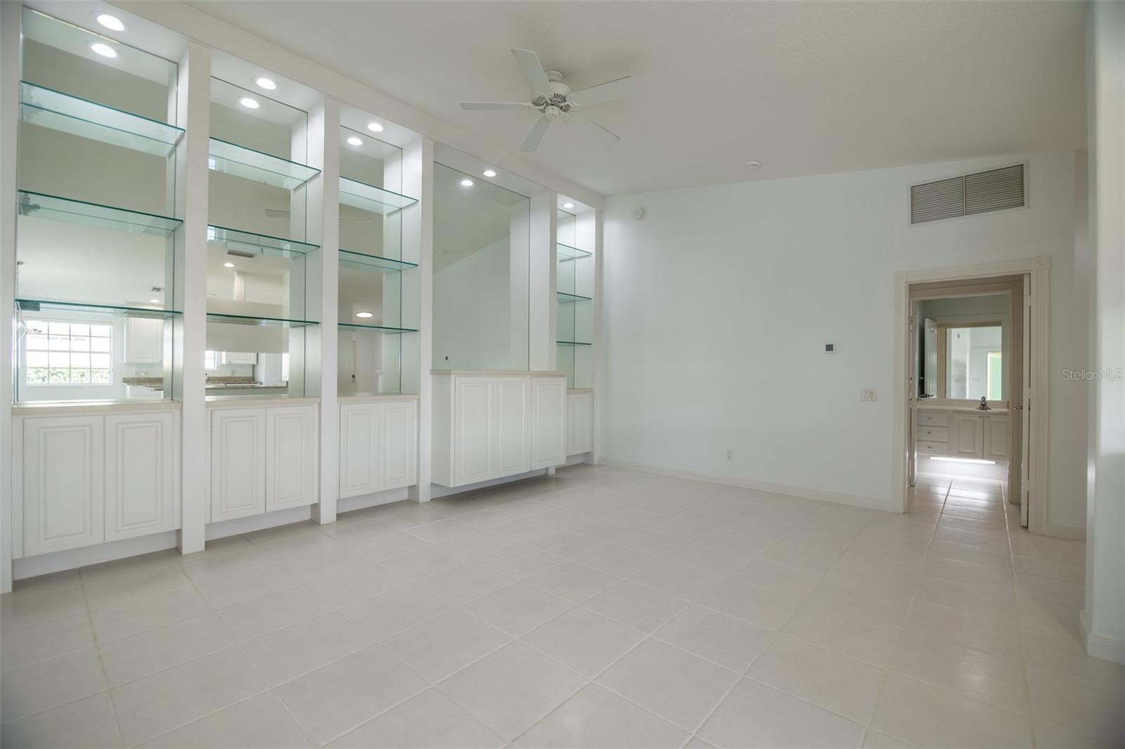 Vacant tiled room with white cabinetry, mirrored panels, and glass display shelves.