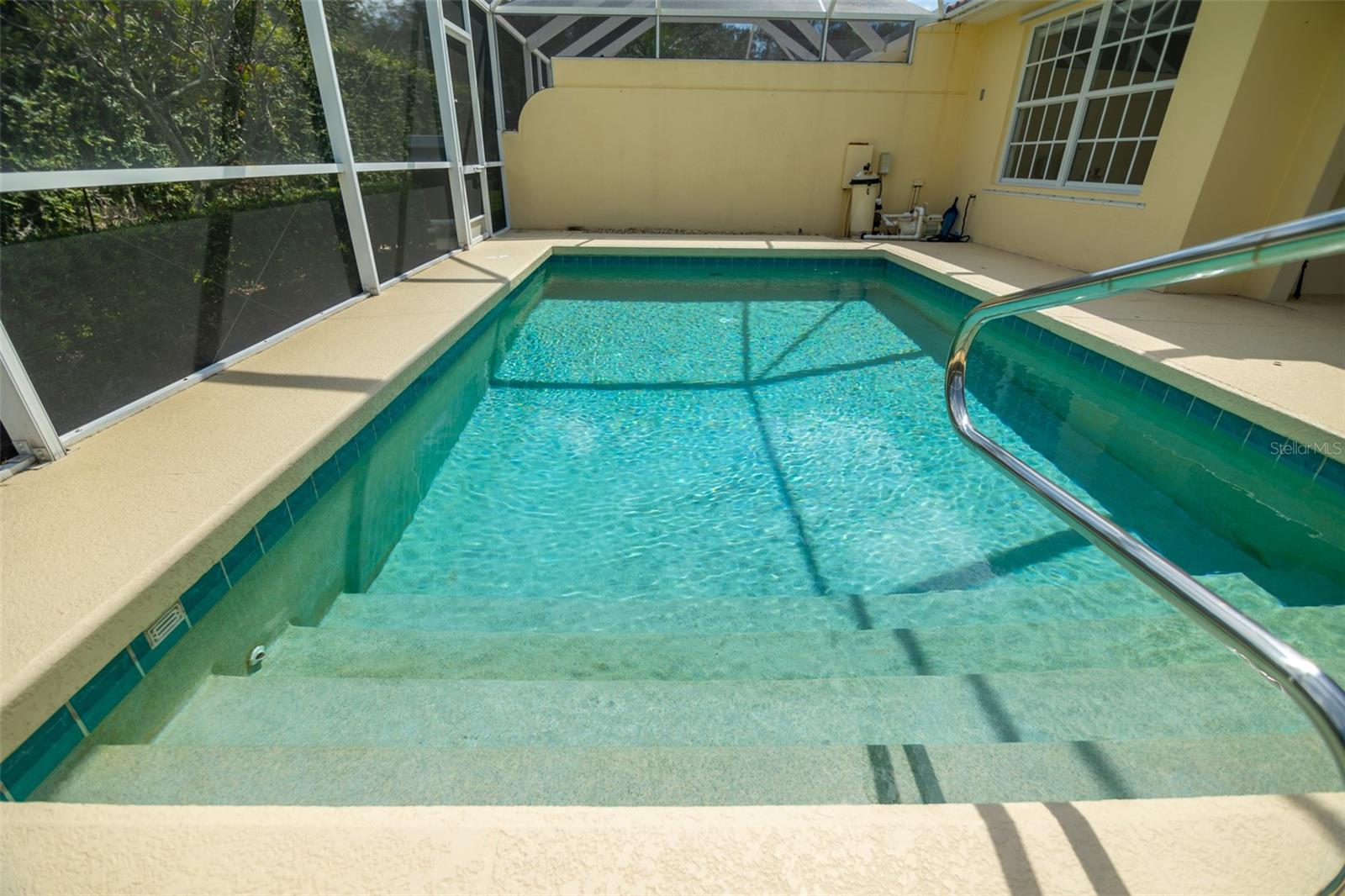Screened-in swimming pool with broad entry steps and a stainless-steel handrail.