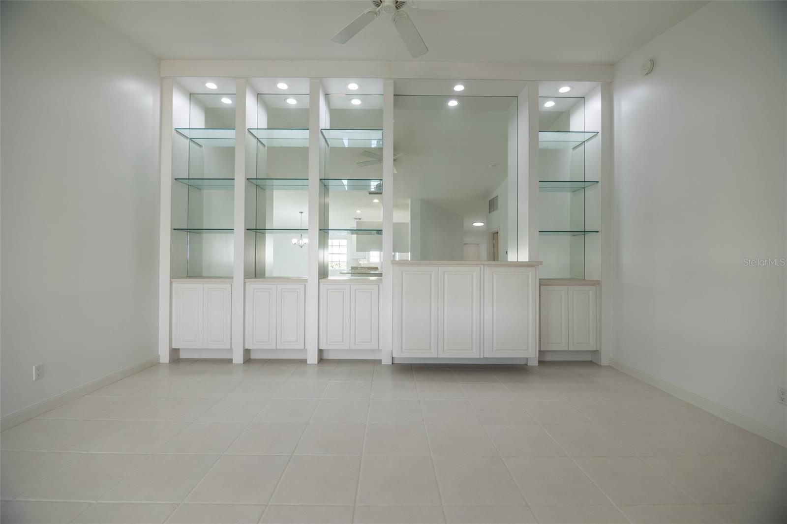 Empty tiled room with built-in white cabinetry, glass shelves, and a counter.