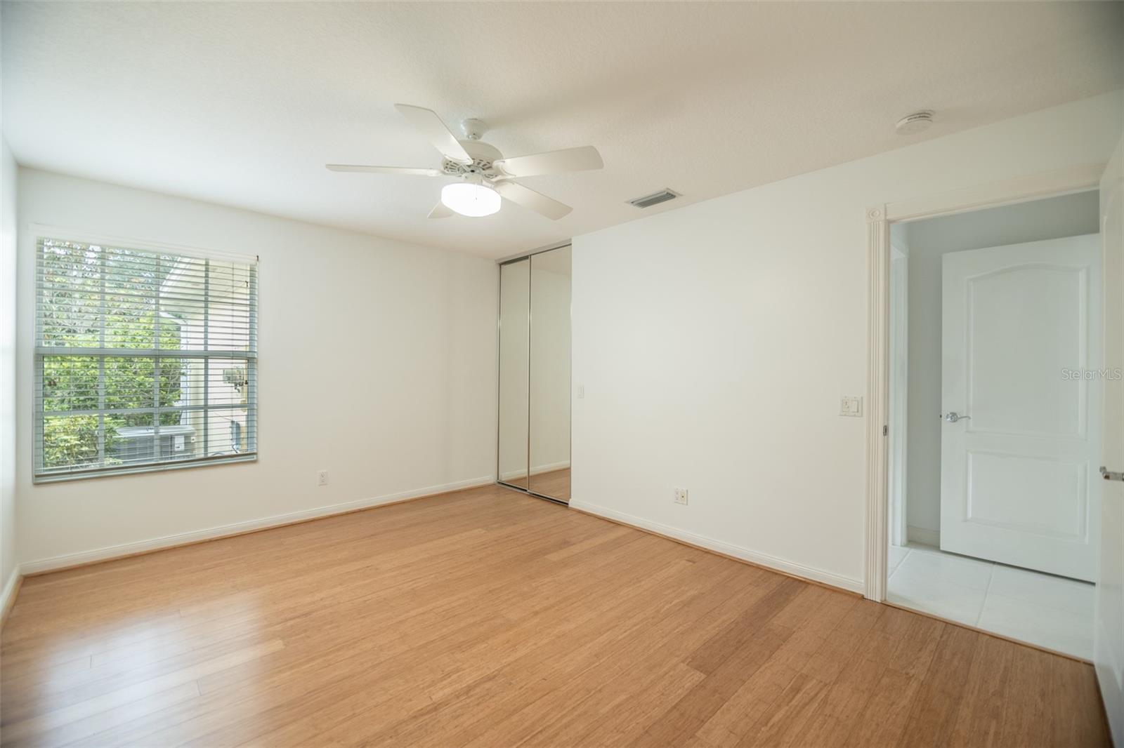 Vacant bedroom with wood flooring, a ceiling fan, and mirrored closet doors.