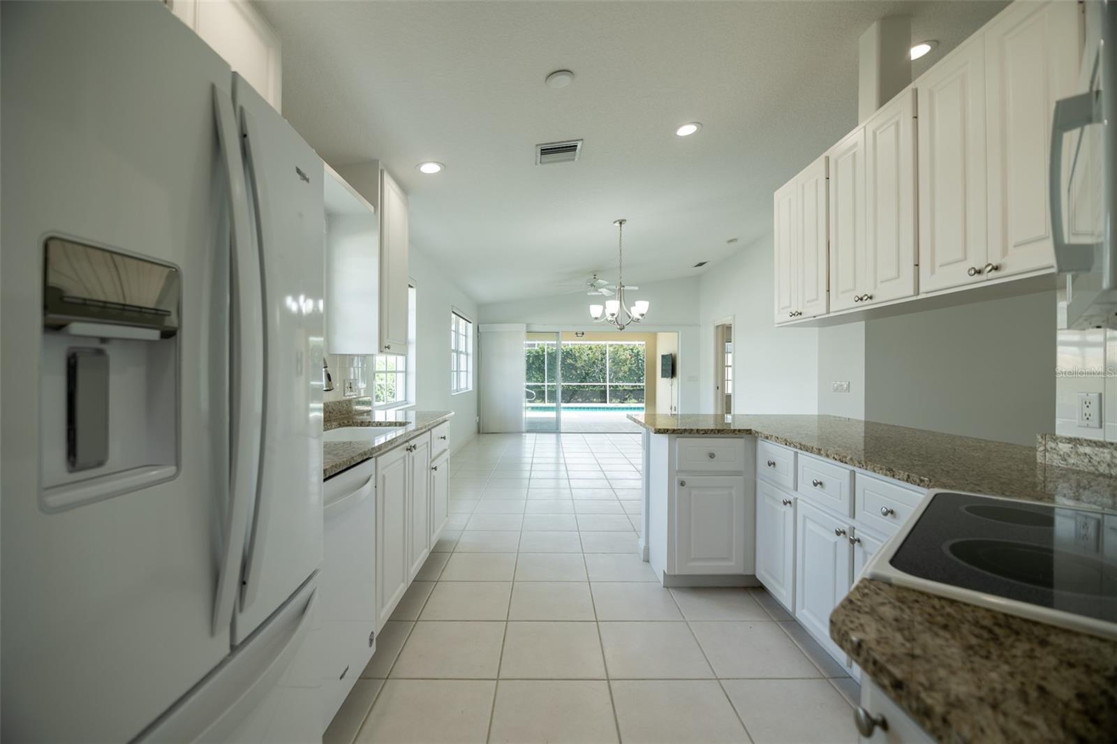 Kitchen with white cabinets and granite counters overlooking sliding doors and a backyard pool.