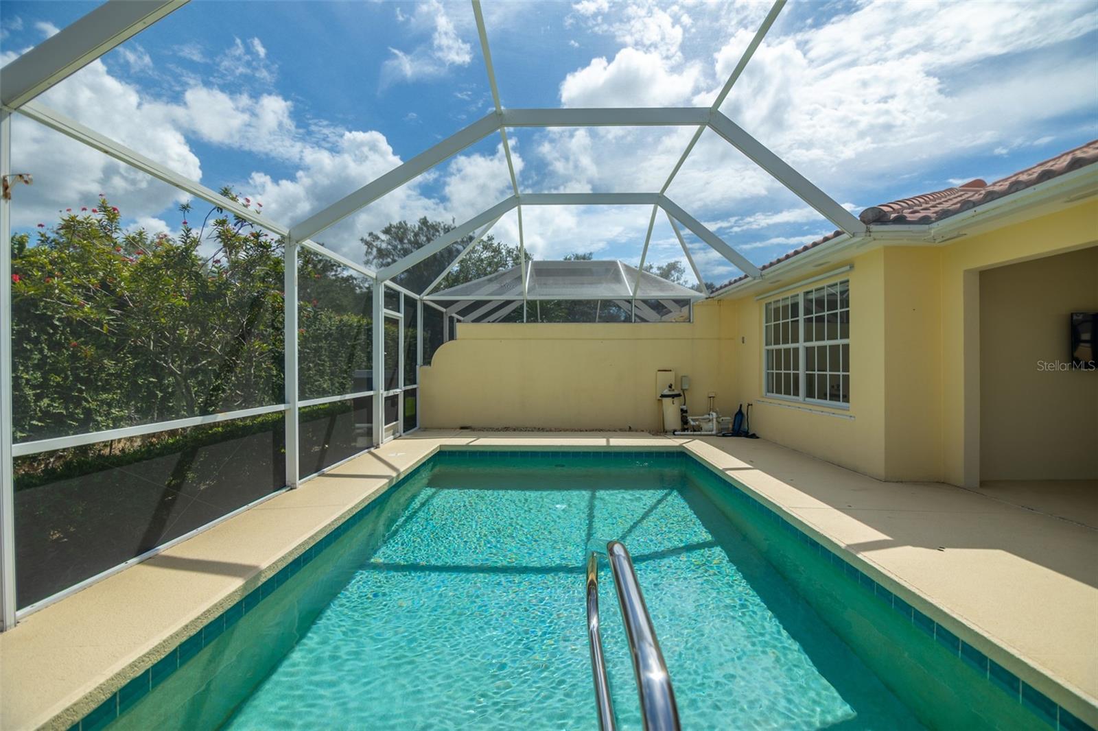 Screened-in backyard pool with turquoise water, a metal handrail, and a light-colored pool deck.