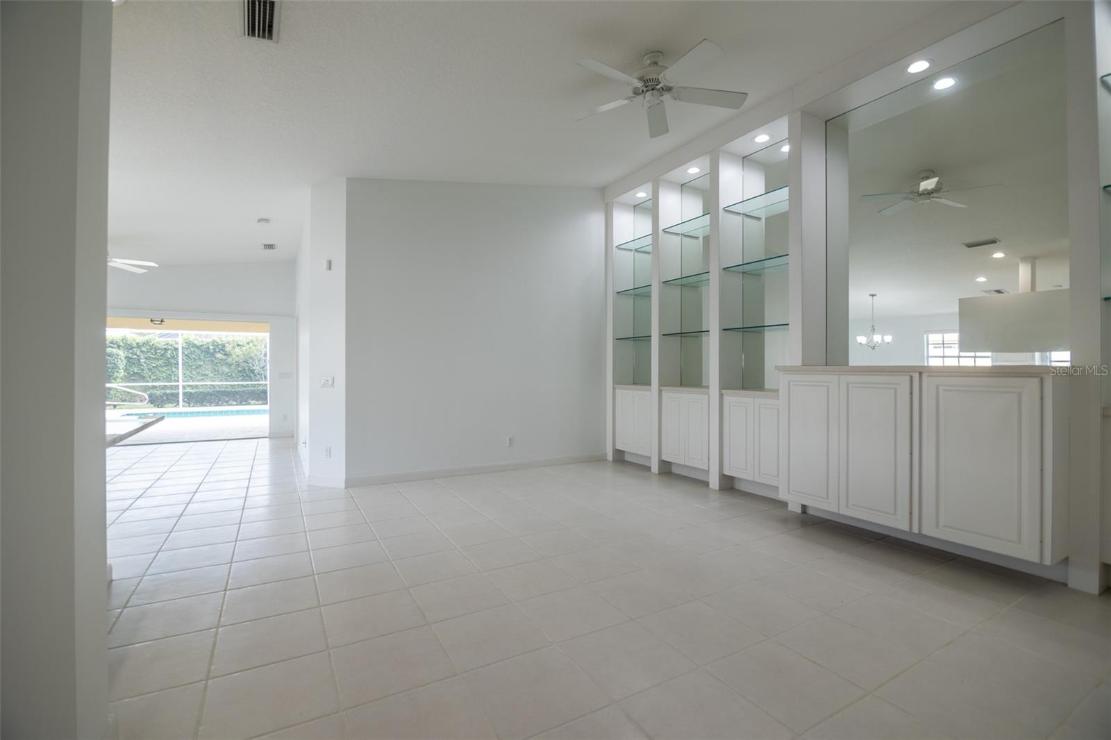 Bright tiled dining area with a white built-in bar and glass shelves, opening toward the pool.