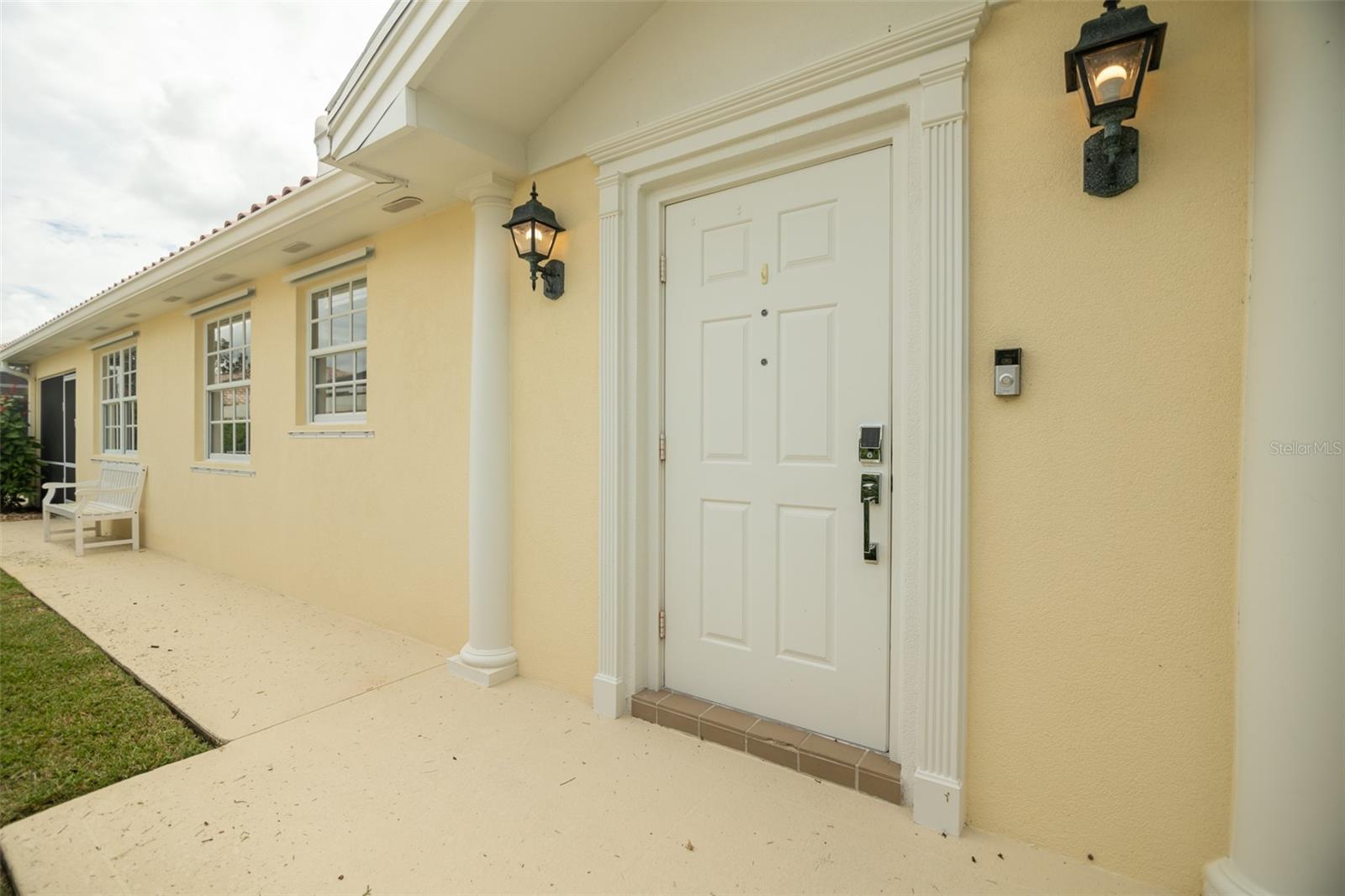 Pale yellow home entrance with a white paneled door, decorative trim, and black wall lanterns.