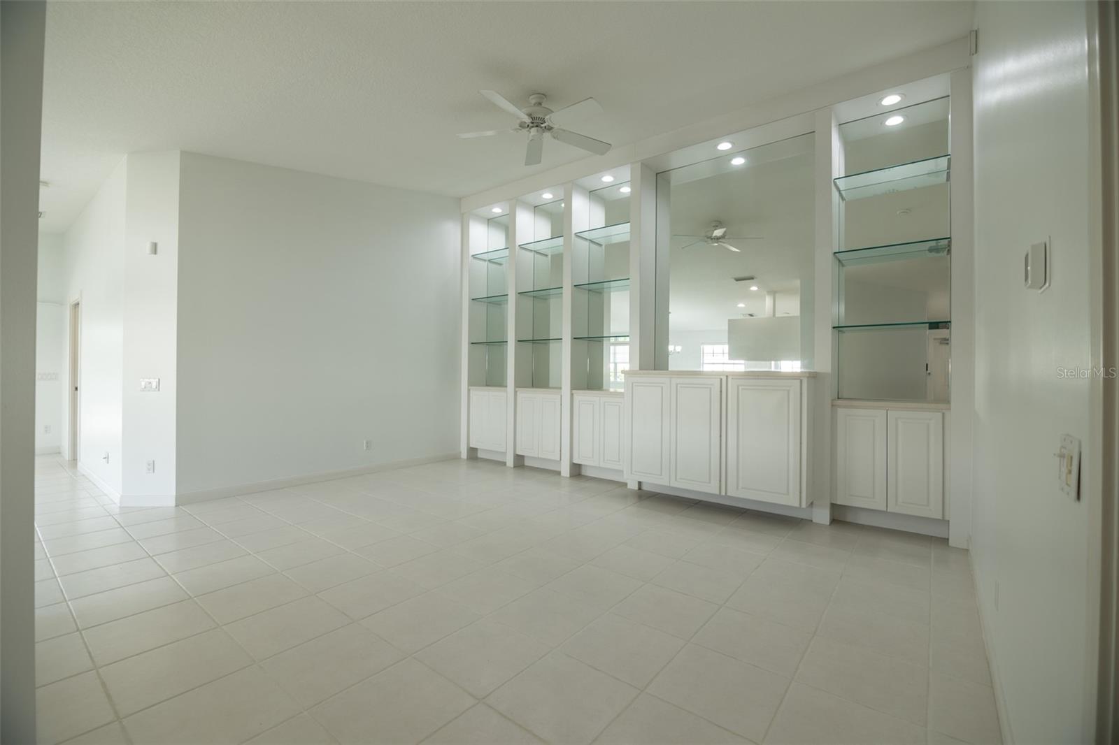 Empty tiled room with built-in white cabinets, glass shelves, and a ceiling fan.
